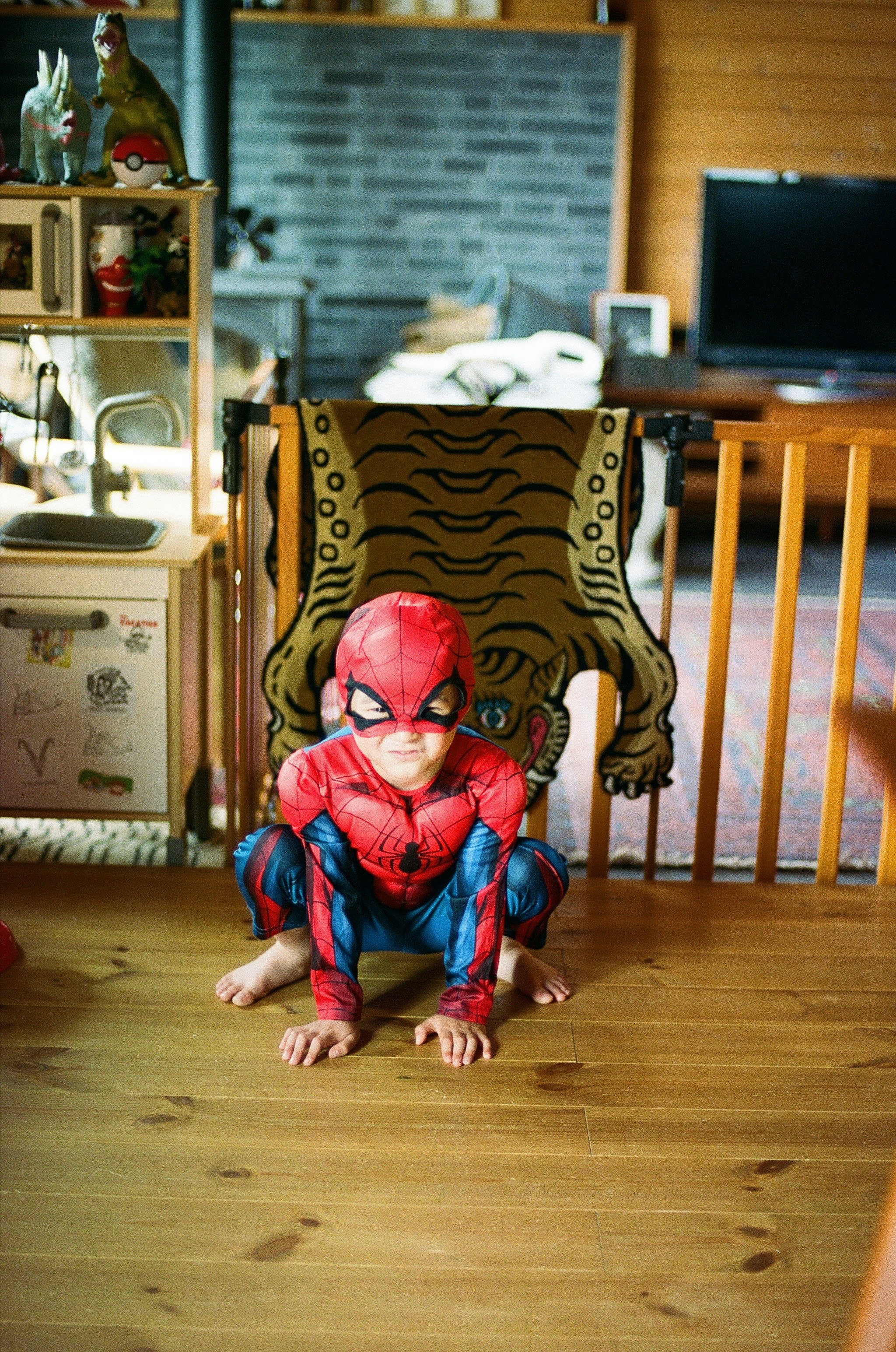 enfant en costume façon Spider-Man posant sur un sol en bois