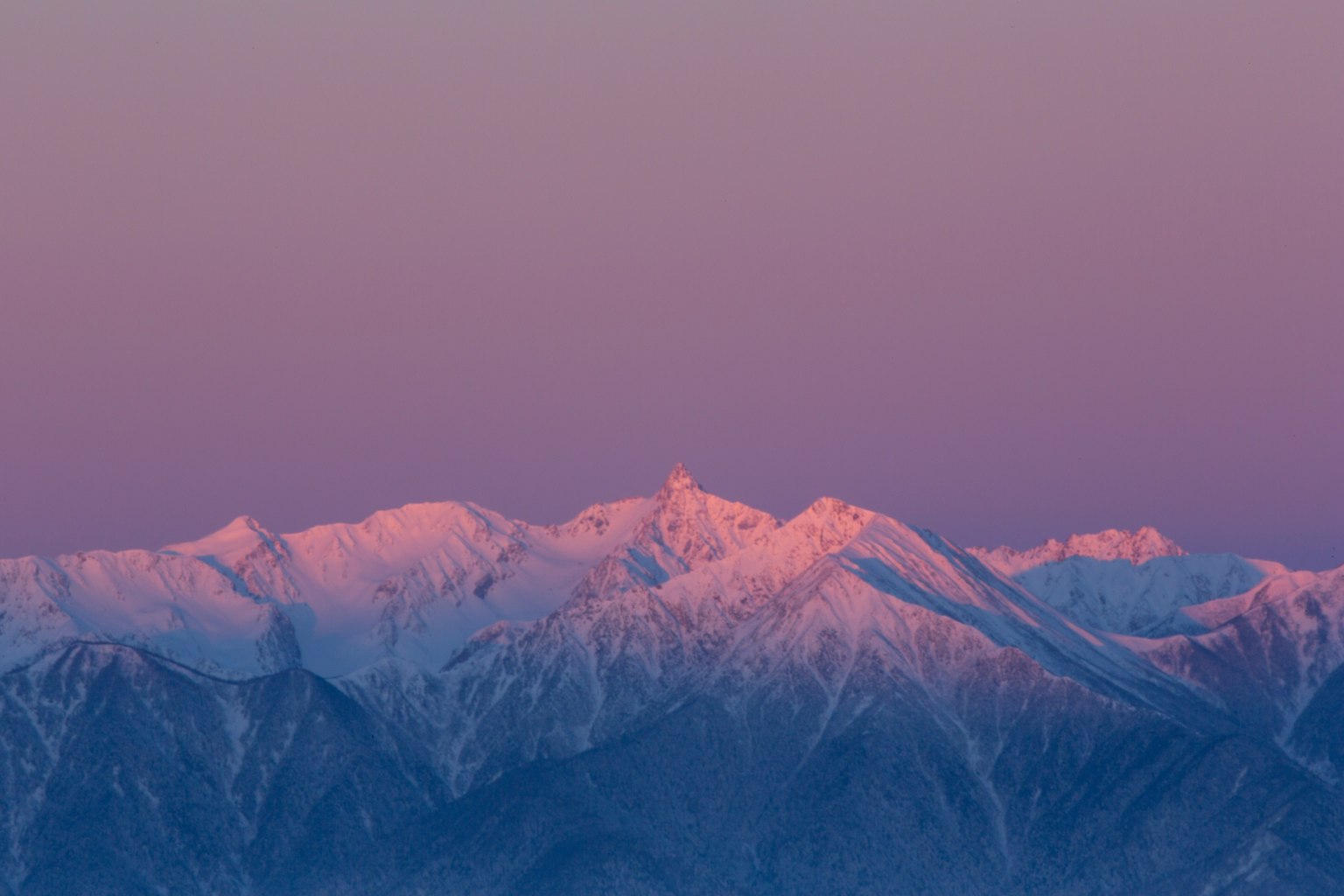 Montagne innevate che si riflettono in un cielo viola al tramonto