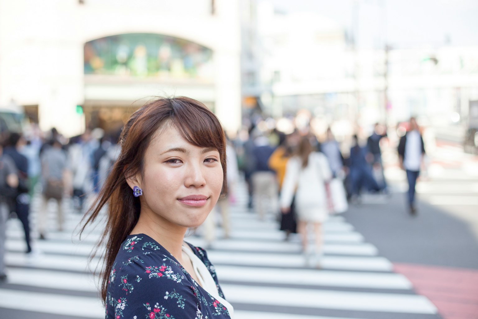 ผู้หญิงยิ้มอยู่บนทางม้าลายพร้อมผู้คนเดินอยู่เบื้องหลัง