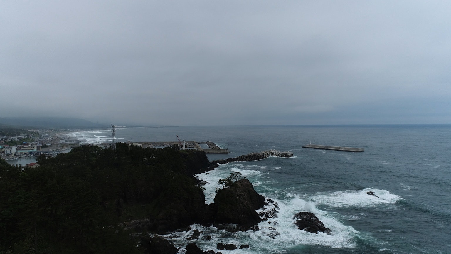 Vista costiera con riva rocciosa e onde che si infrangono cielo nuvoloso e faro in lontananza