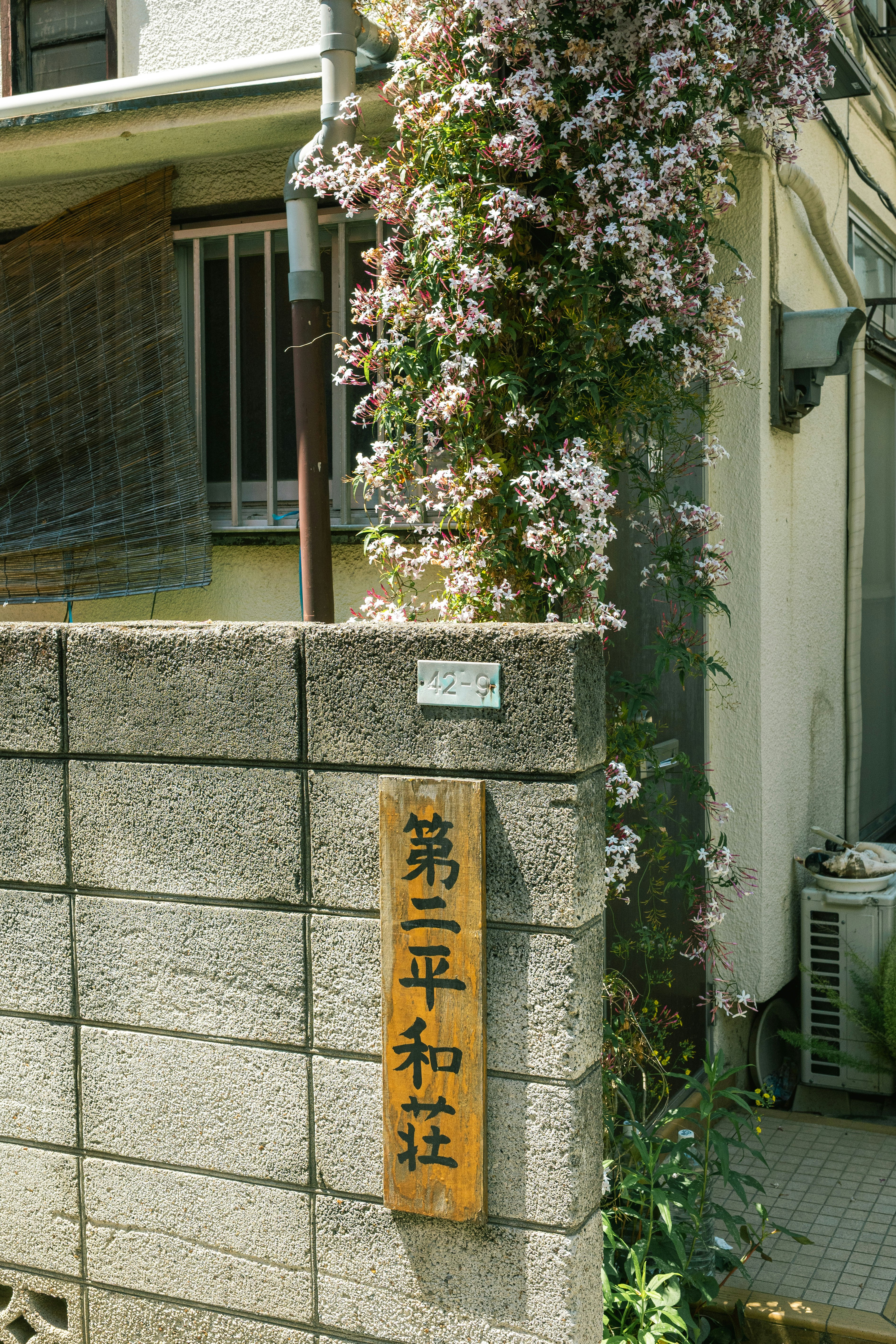 花で覆われた石壁と木製の看板が特徴の住宅の入口
