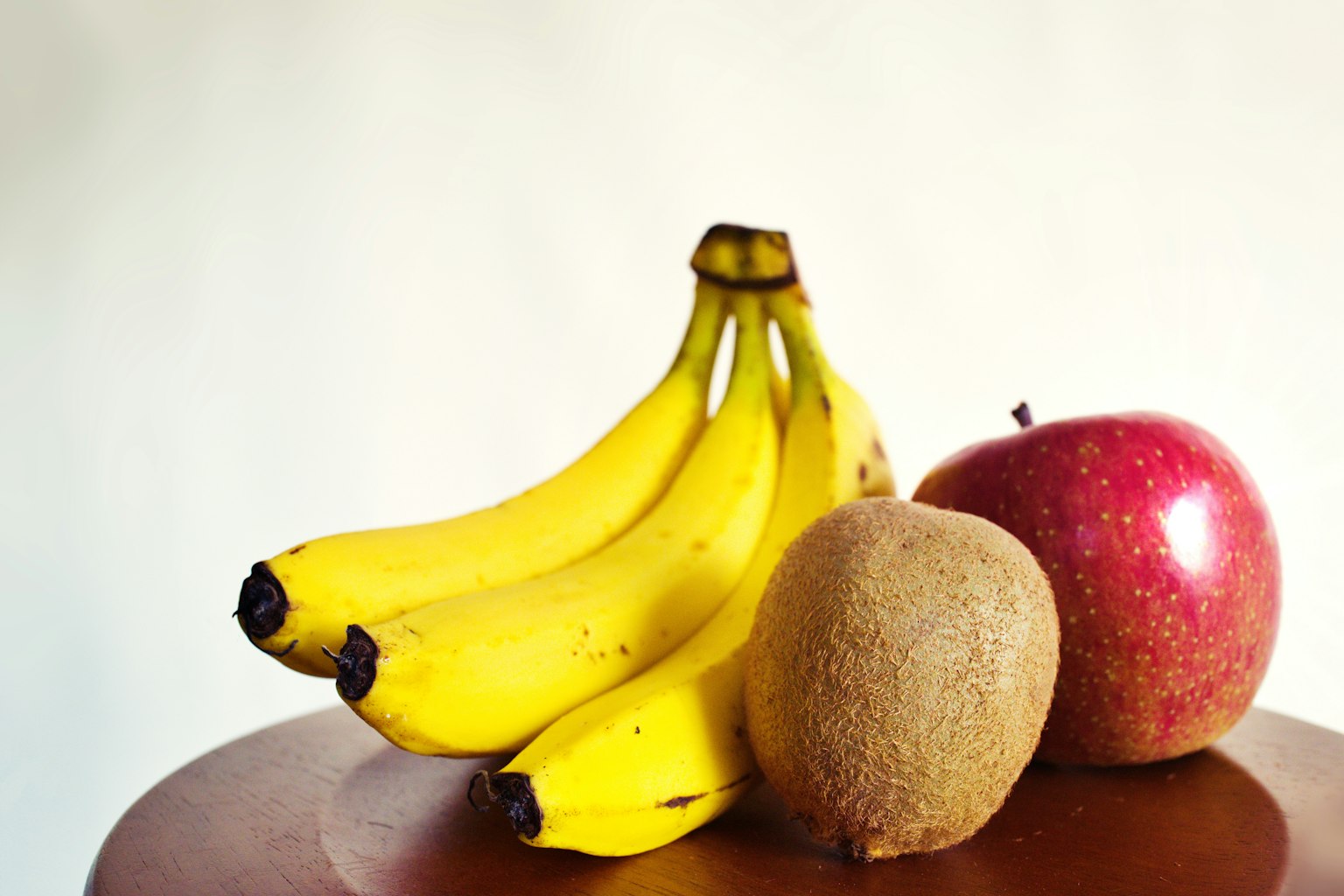 Une grappe de bananes jaunes une pomme rouge et un kiwi brun sur une table en bois