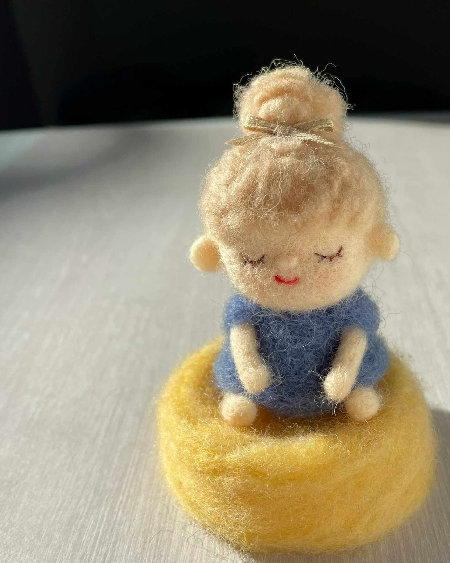 Une poupée en feutre assise sur une base jaune avec une robe bleue et un chignon