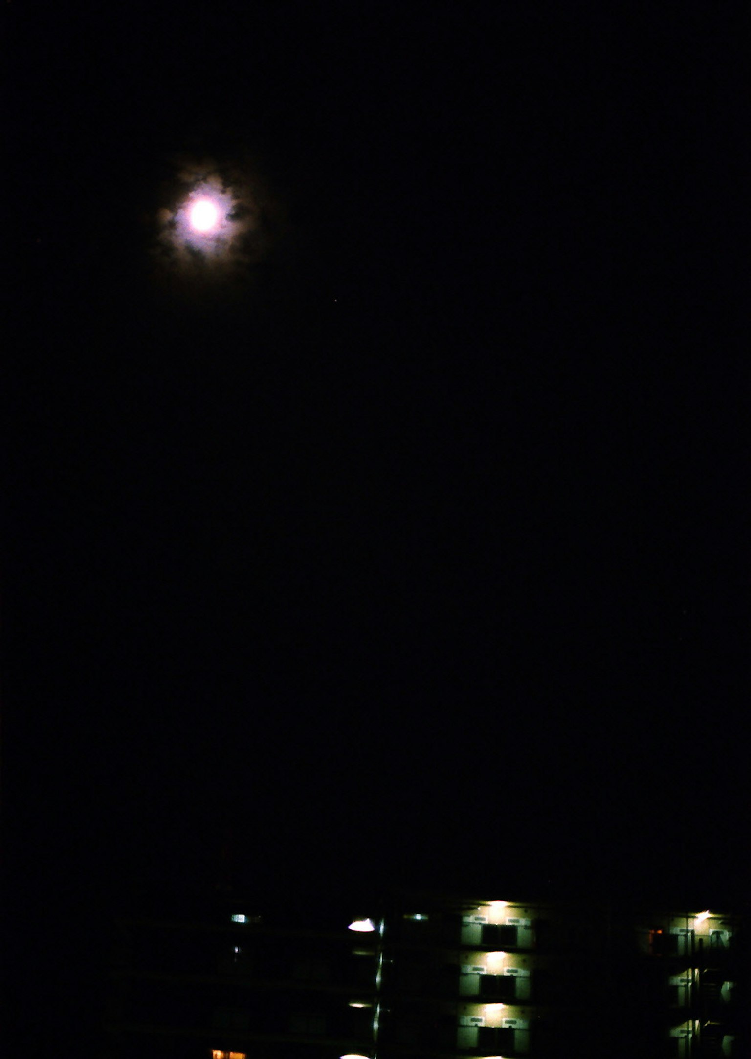 Luna llena brillante en el cielo nocturno con siluetas oscuras de edificios