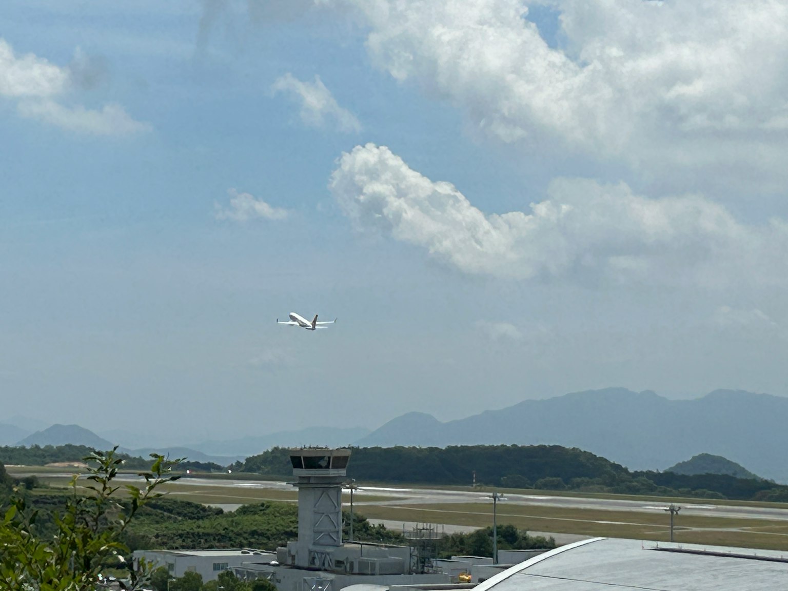 An airplane taking off with an airport tower and mountains in the background