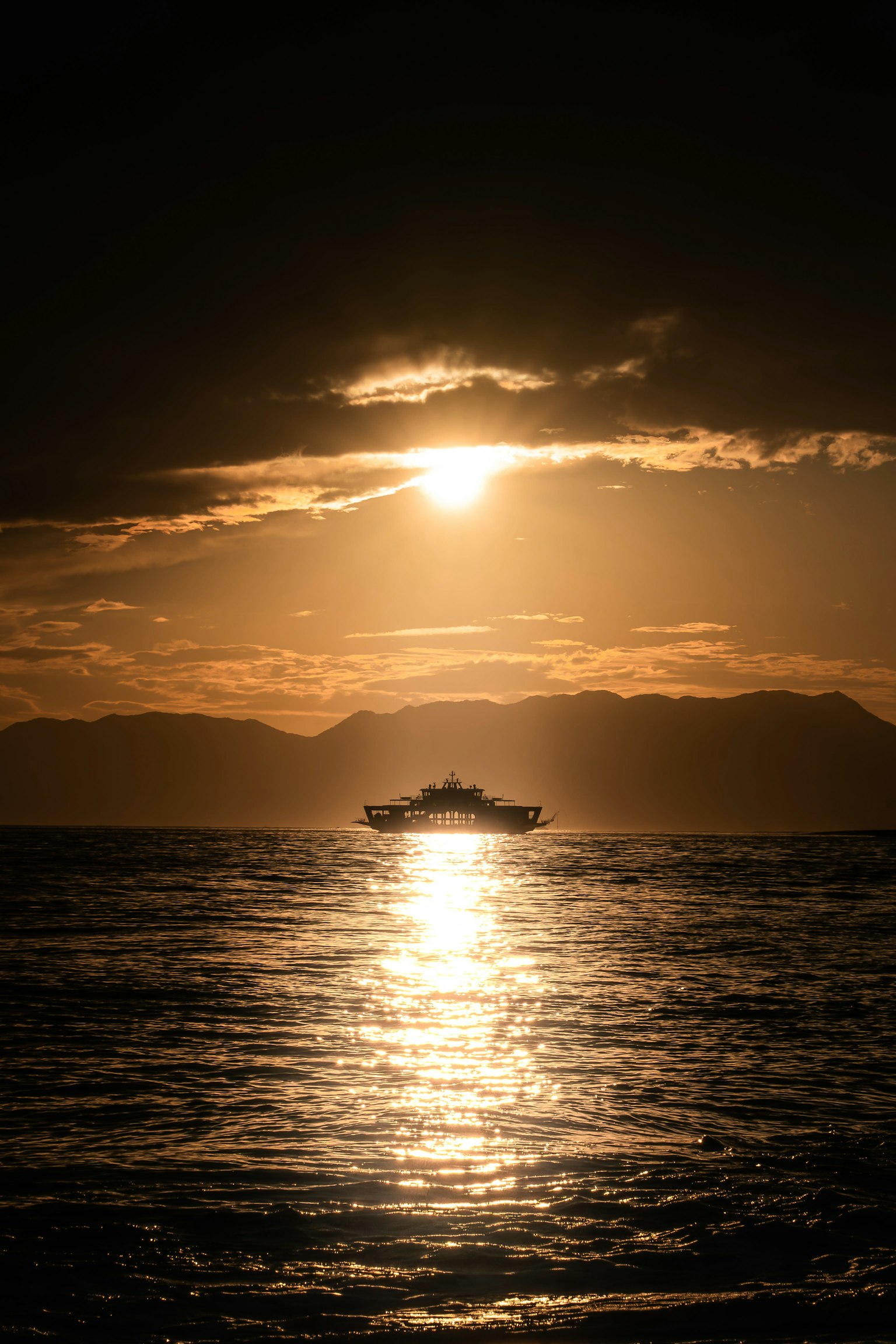 Silhouette d'un bateau sur l'océan au coucher du soleil avec des reflets sur l'eau