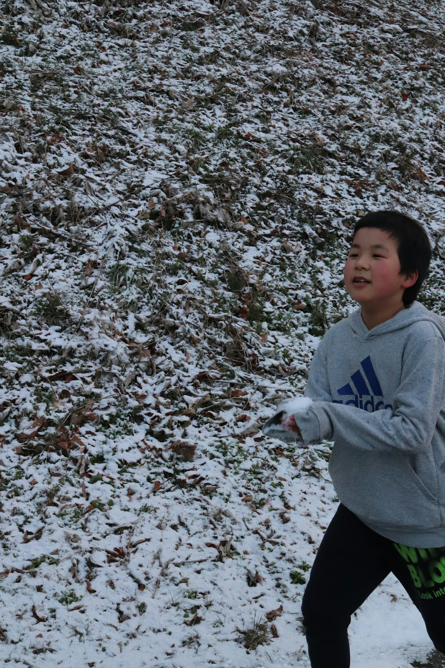 Boy running in the snow wearing a gray hoodie