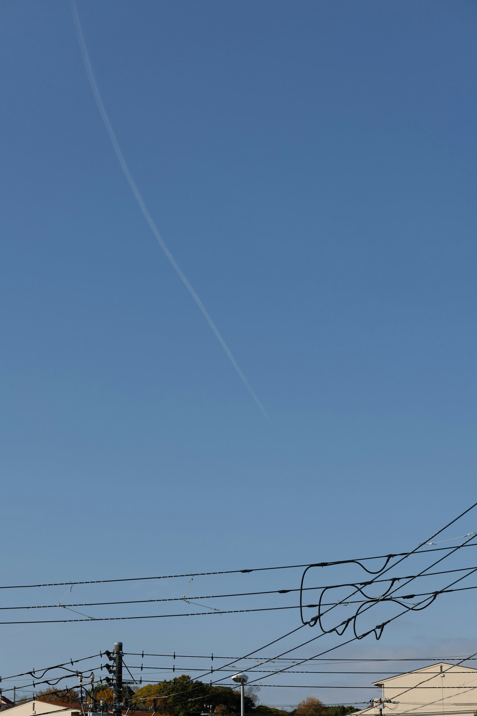 青空に飛行機雲と電線が見える風景
