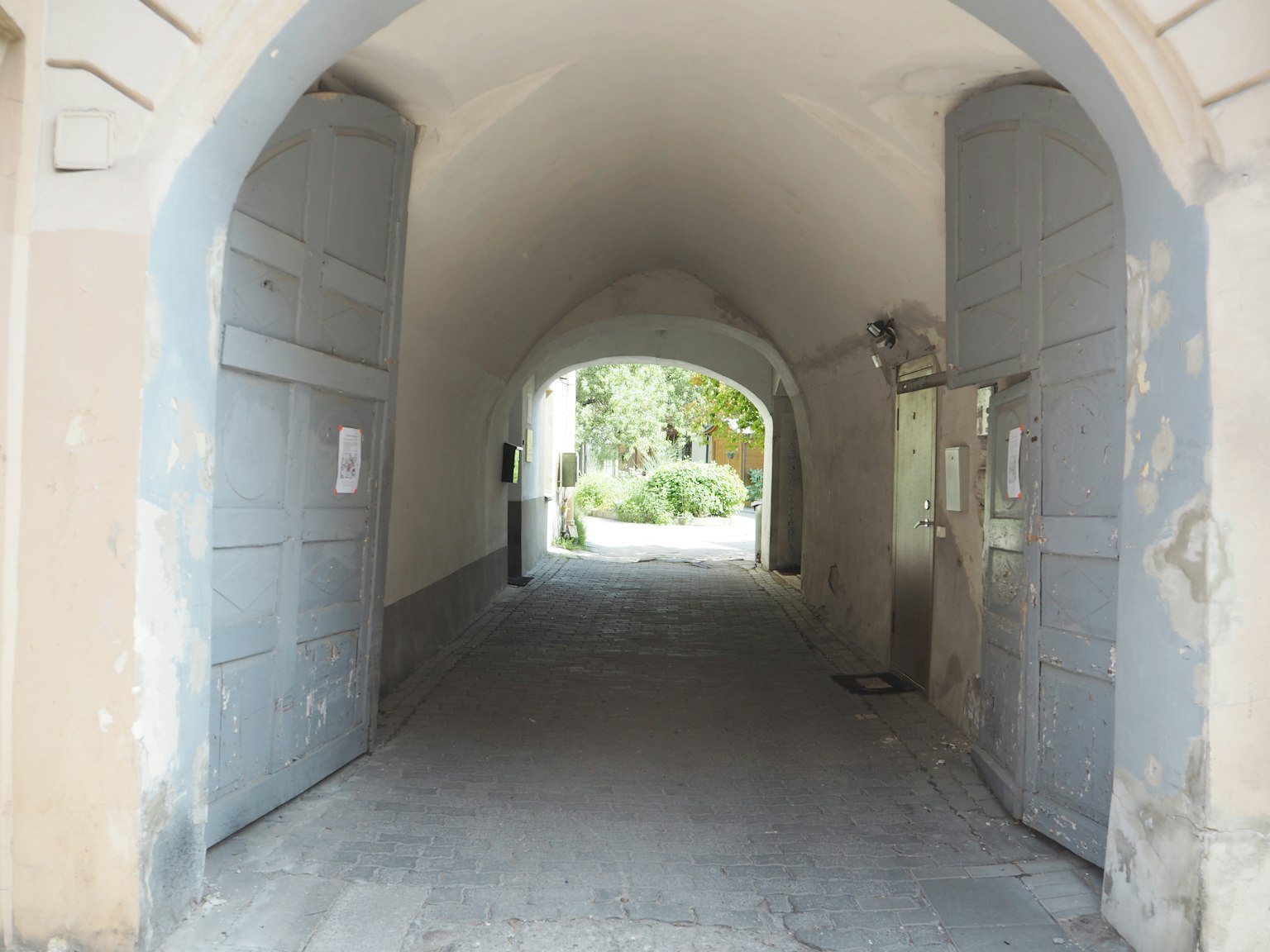 Lorong melengkung yang mengarah ke taman hijau dengan dinding dan pintu yang usang
