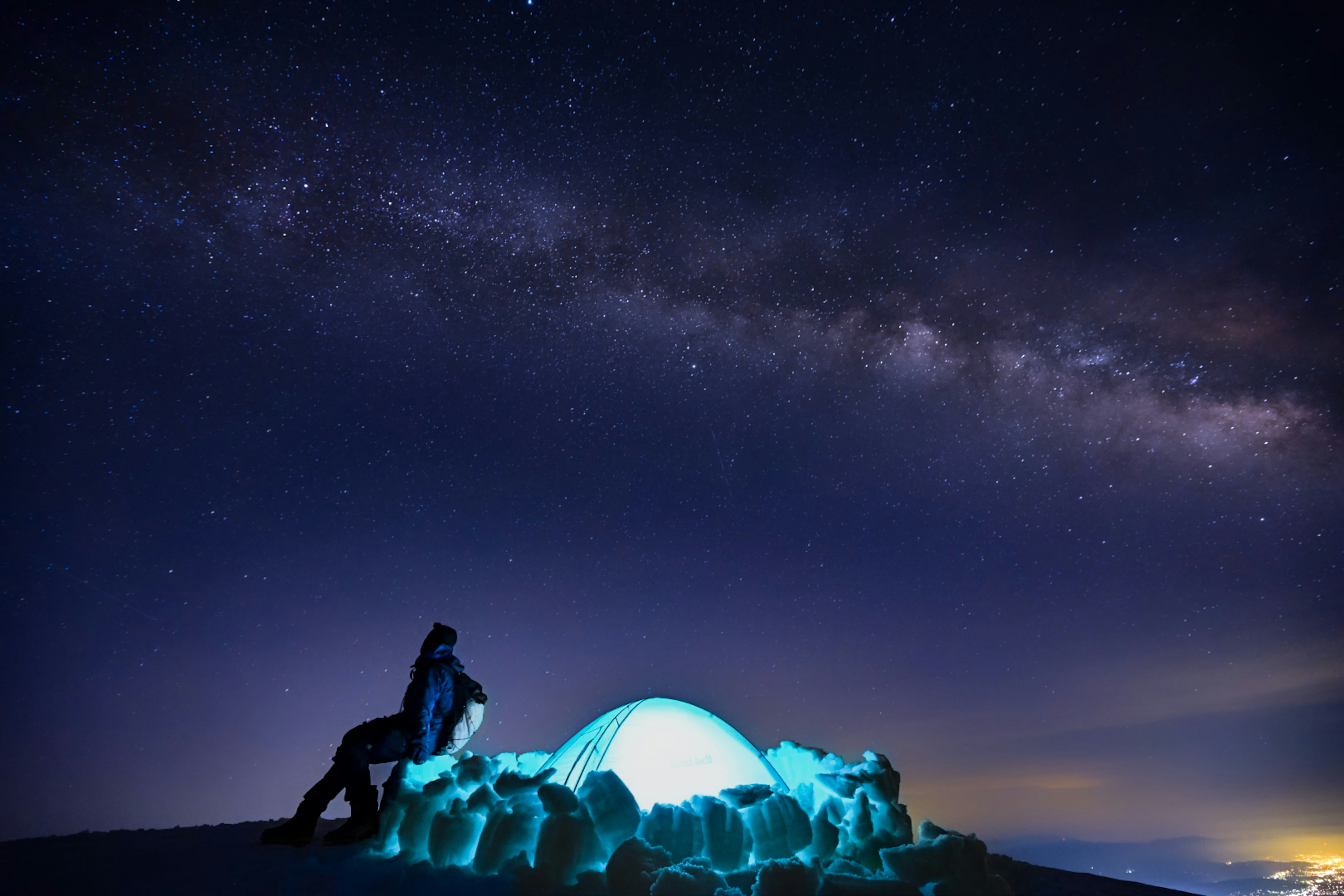 夜空の星空と銀河を背にした人物と青い光の岩