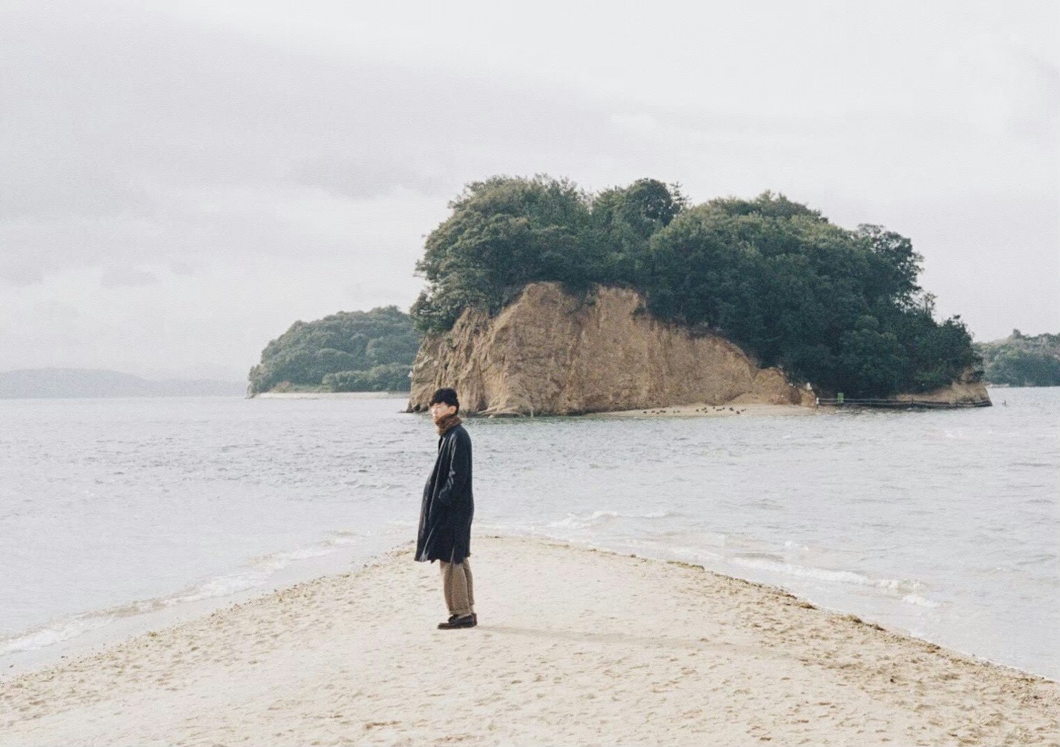 一個人站在海邊的沙灘小道上，背景是一個小島
