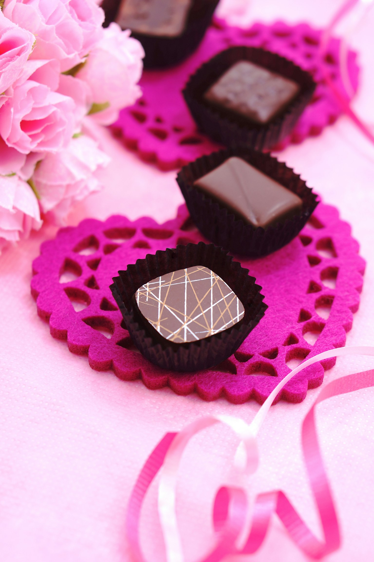 Deliziosi cioccolatini disposti su un tappetino a forma di cuore rosa con un bouquet di fiori