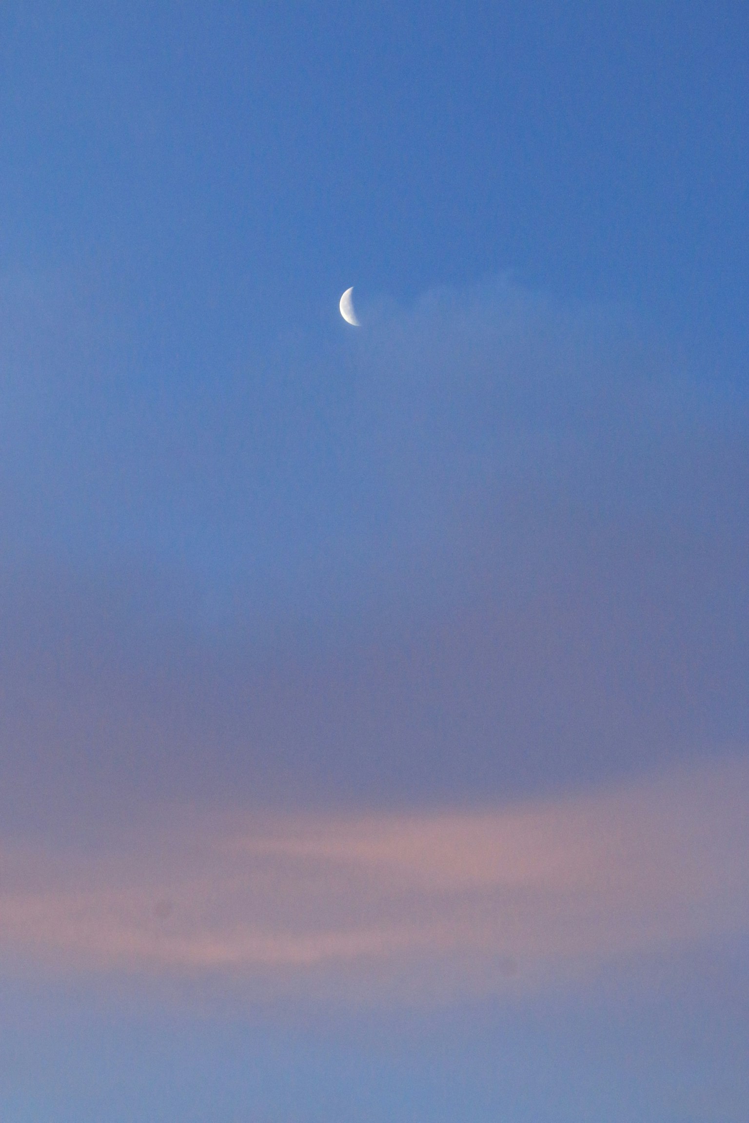 Una luna crescente in un cielo blu con nuvole morbide