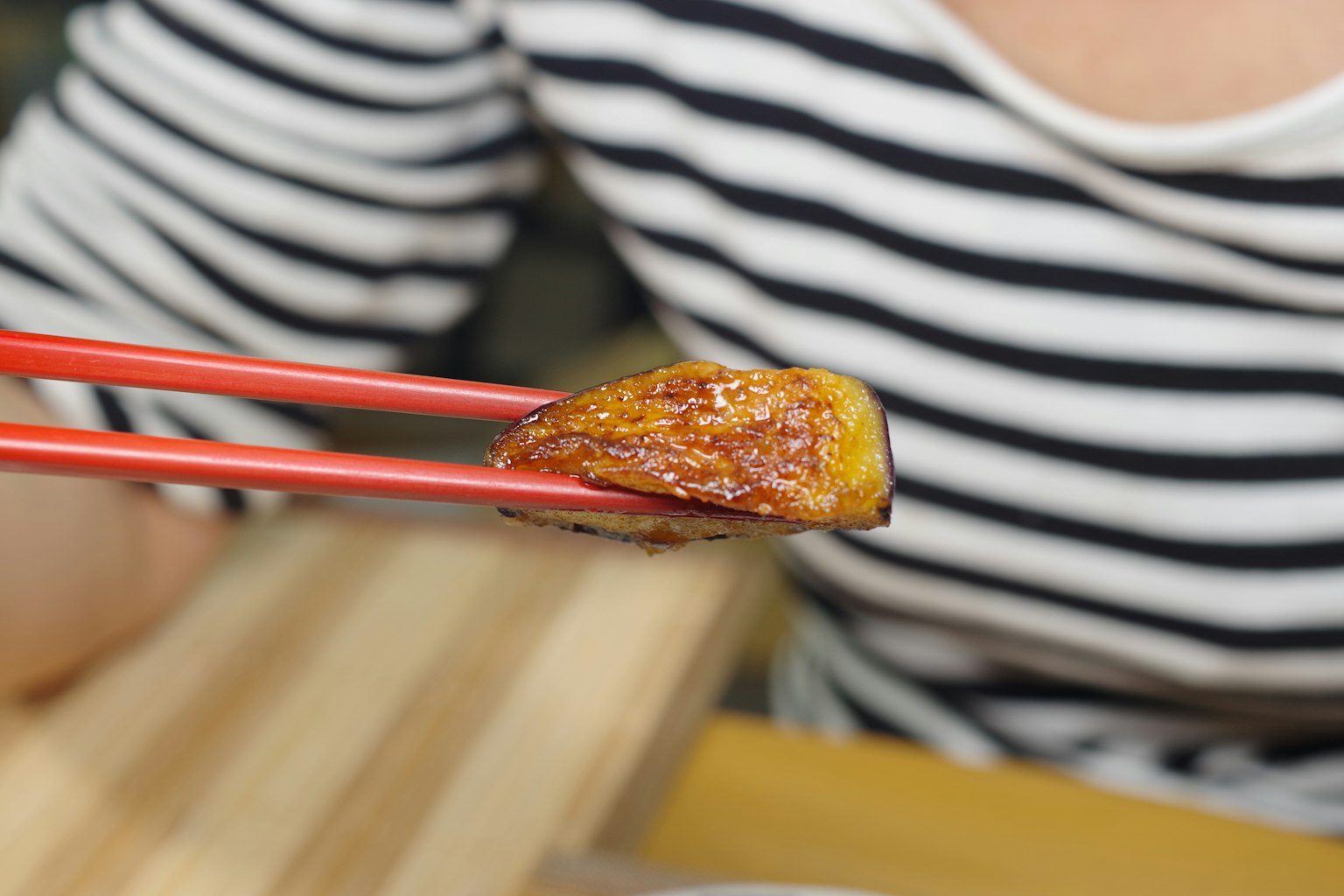 Un morceau de poisson grillé tenu avec des baguettes rouges et une chemise rayée
