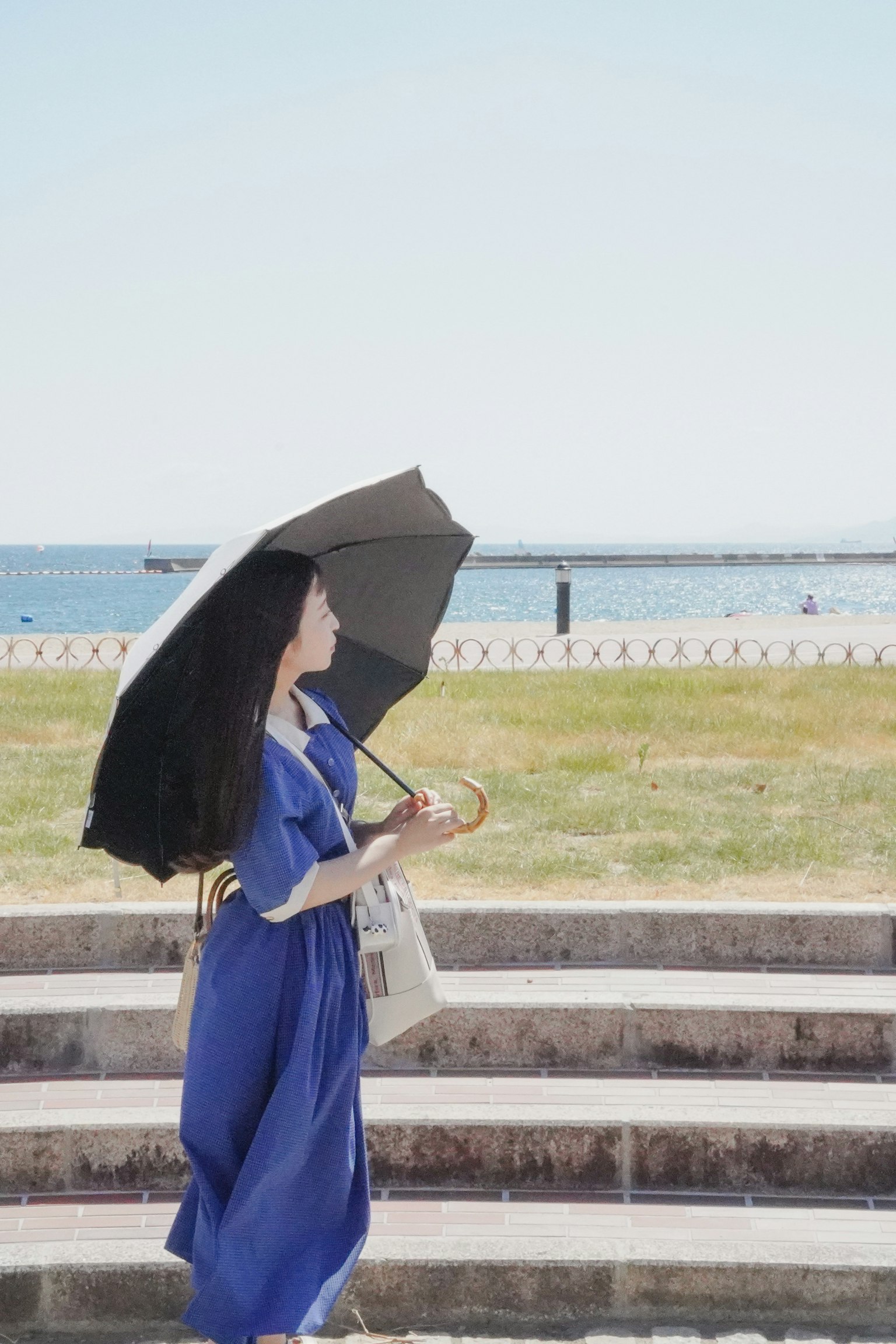 Una donna in abito blu che tiene un ombrello mentre cammina lungo il mare