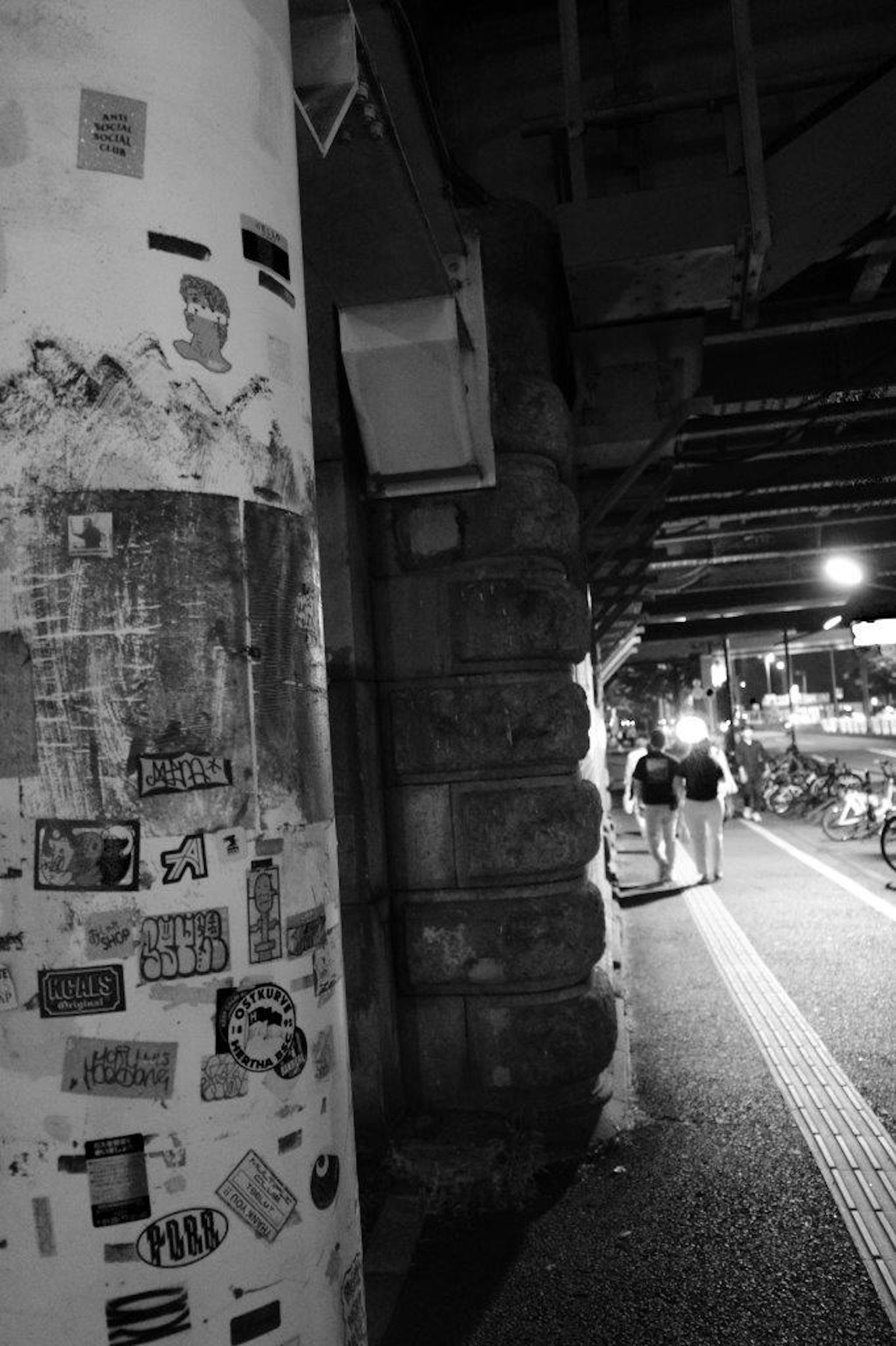 Scena di strada in bianco e nero con un pilastro coperto di manifesti e marciapiede