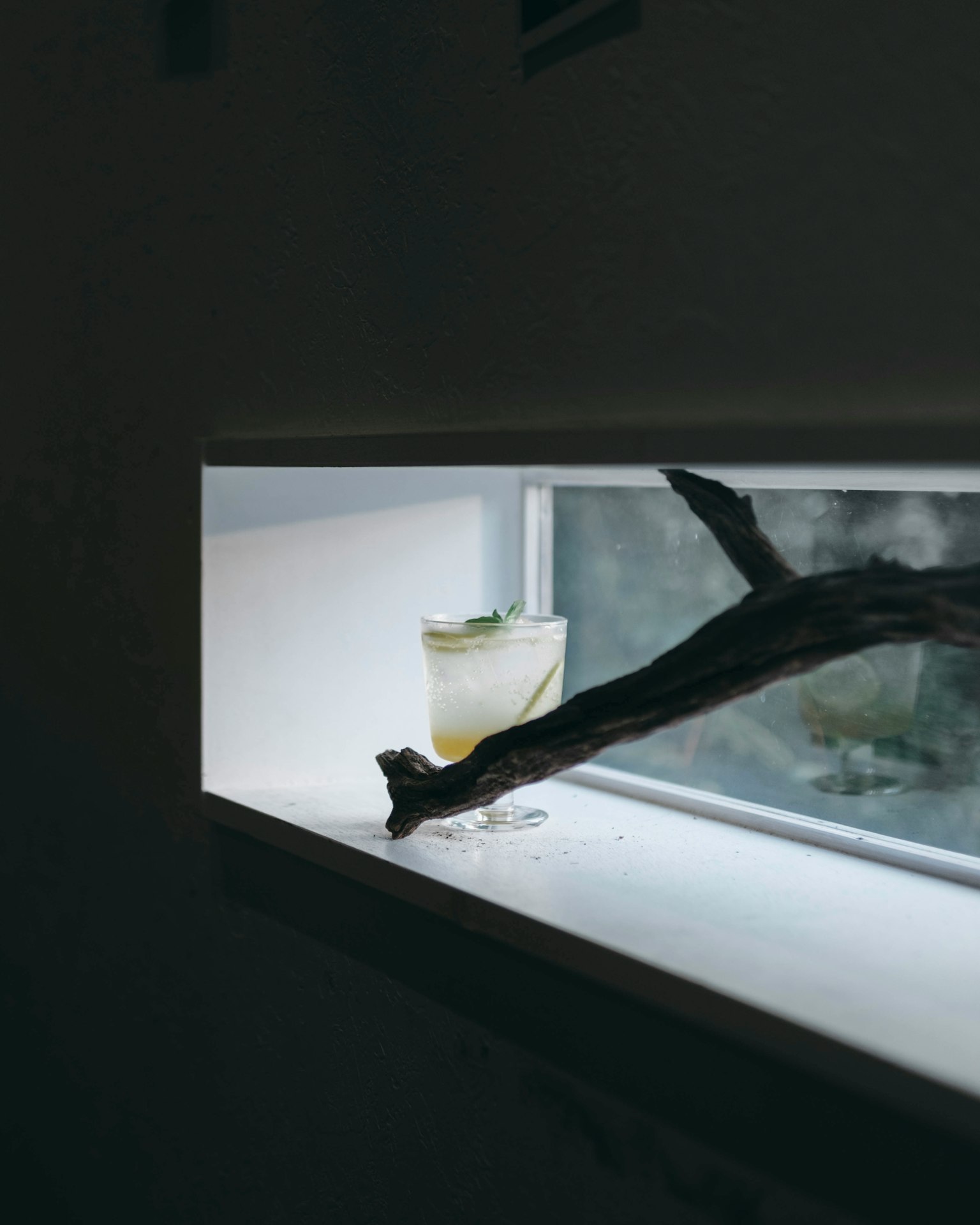 Un bicchiere di cocktail posato su un davanzale luminoso con un ramo naturale