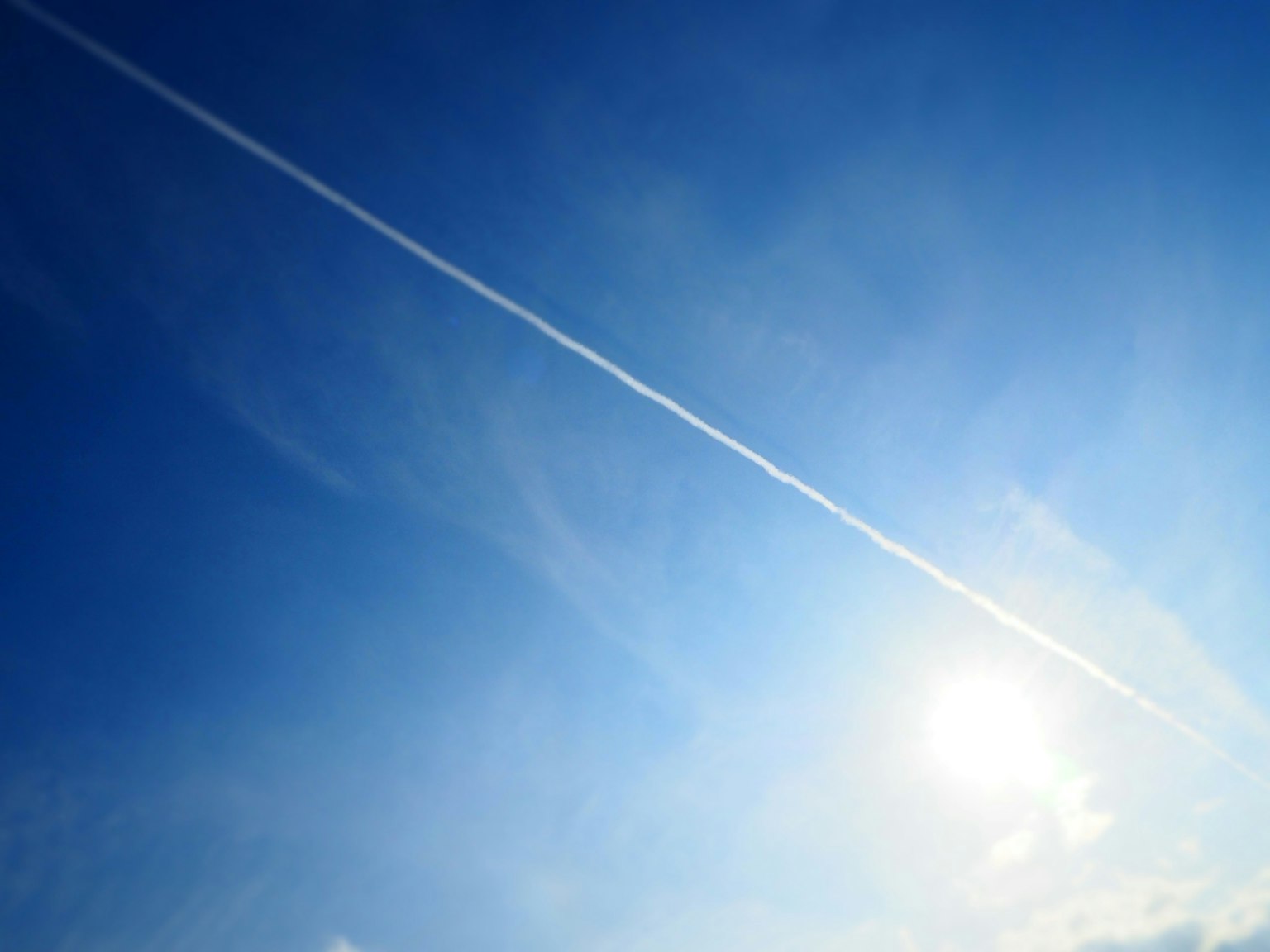 Un cielo blu chiaro con una scia bianca e il sole