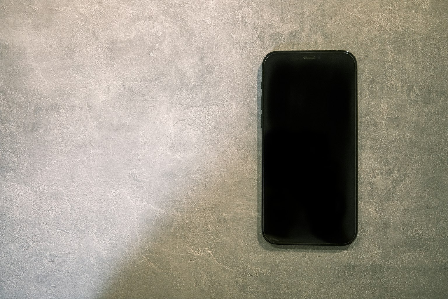 Schwarzes Smartphone an einer grauen Wand