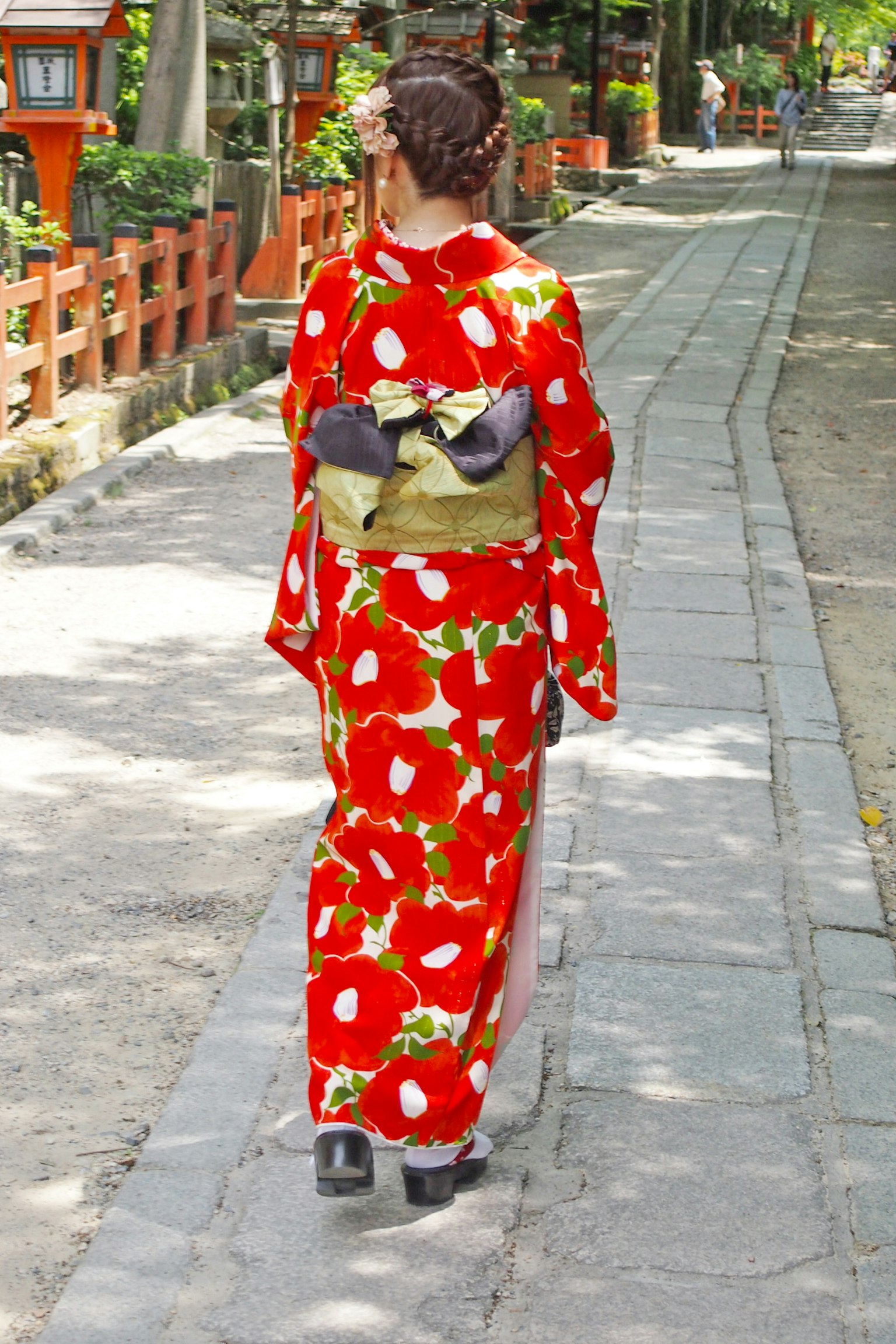 穿著紅色花卉和服的女人走在石頭小路上