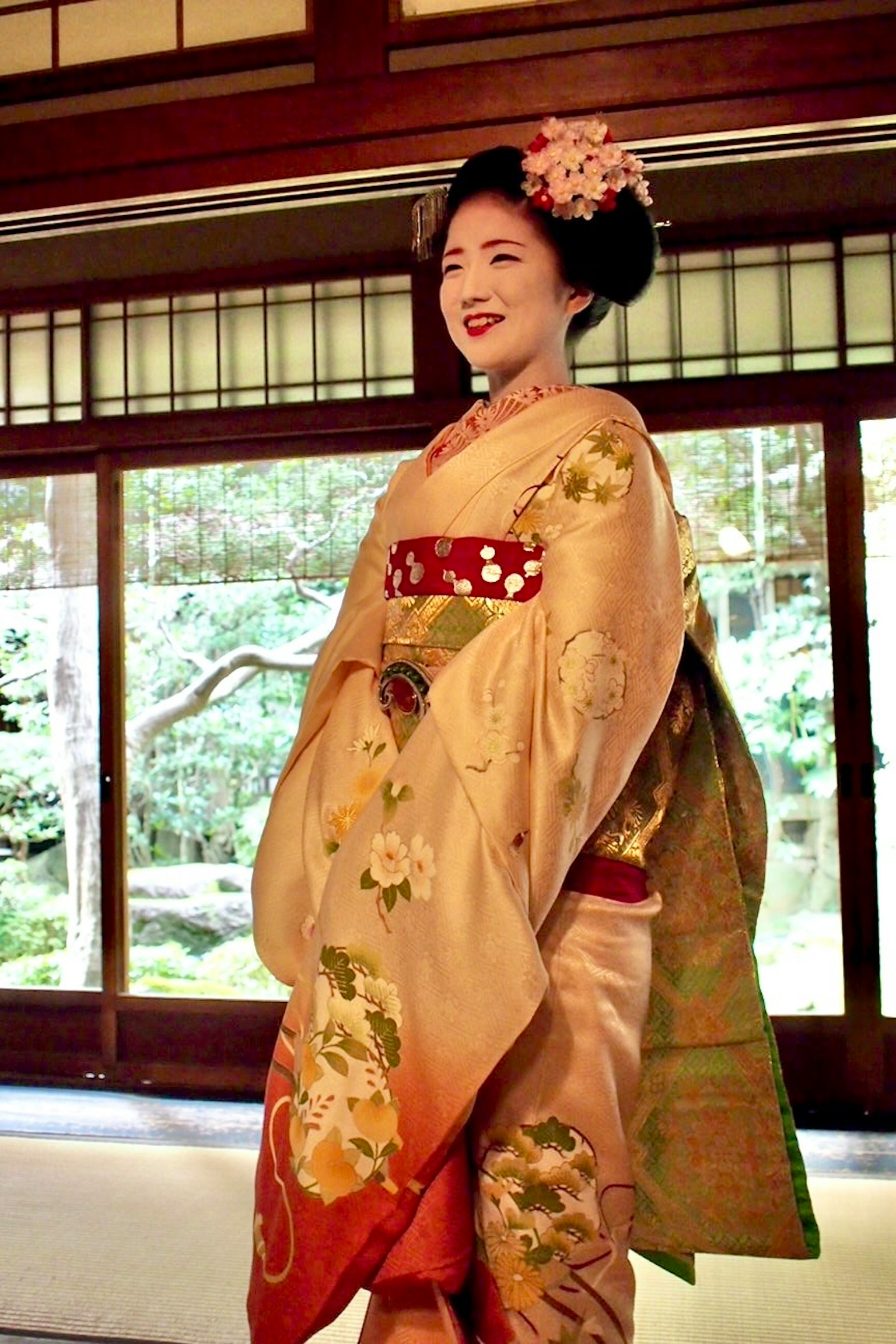 Một người phụ nữ trong trang phục kimono đang mỉm cười trước nền vườn