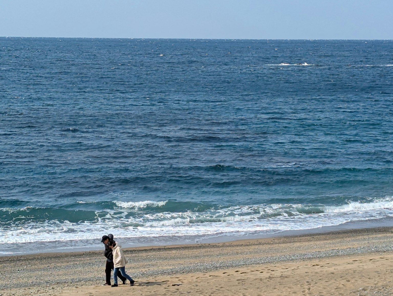 Pasangan berjalan di pantai dengan ombak tenang
