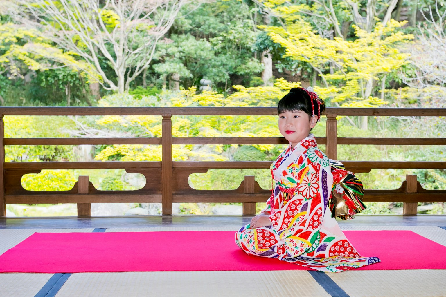 Une jeune fille portant un kimono coloré est assise devant un jardin