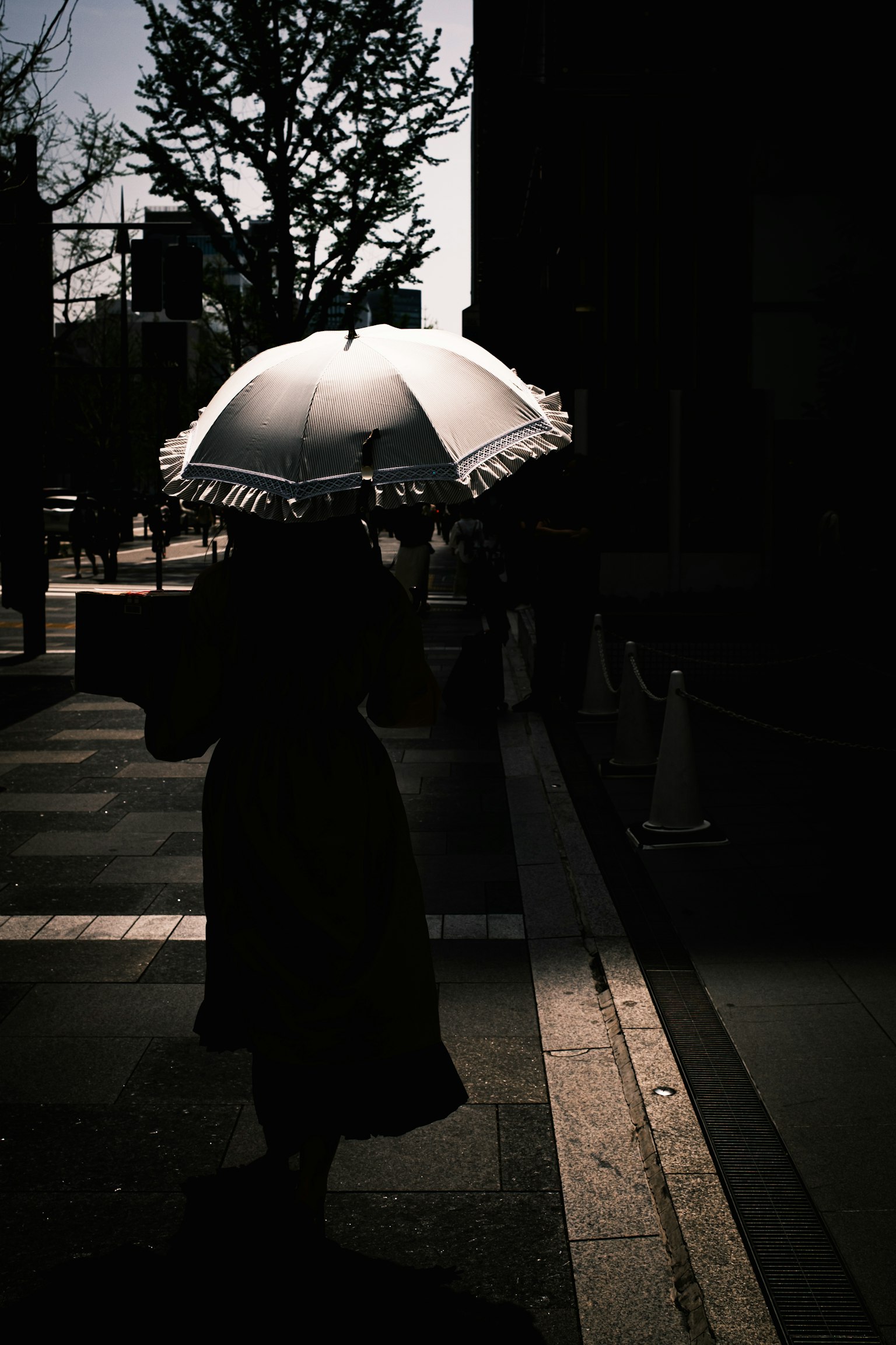 Silhouette di una donna che cammina con un ombrello in una strada di città sotto la luce del sole