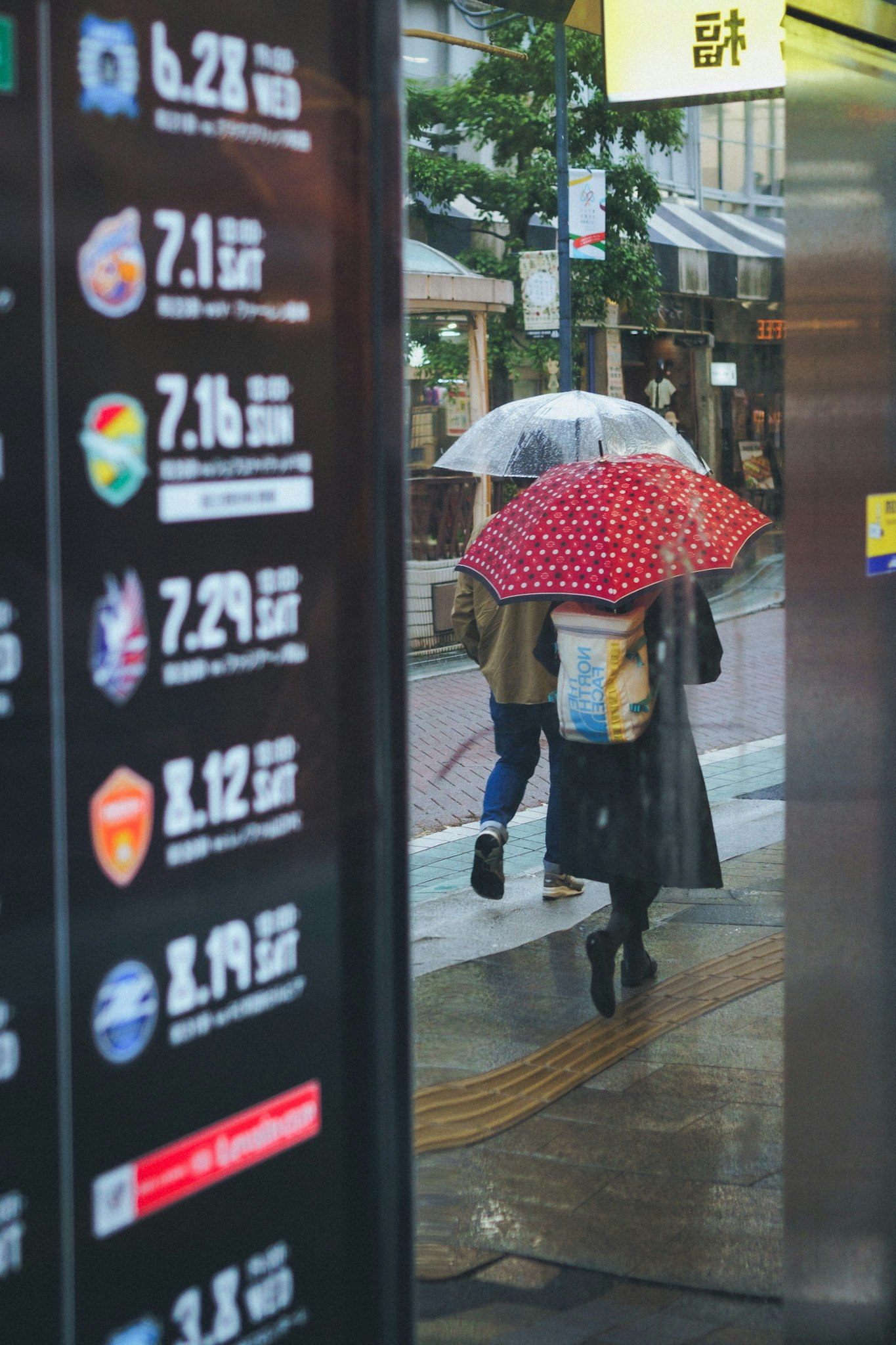 雨の日の路地で傘をさす人と掲示板の数字