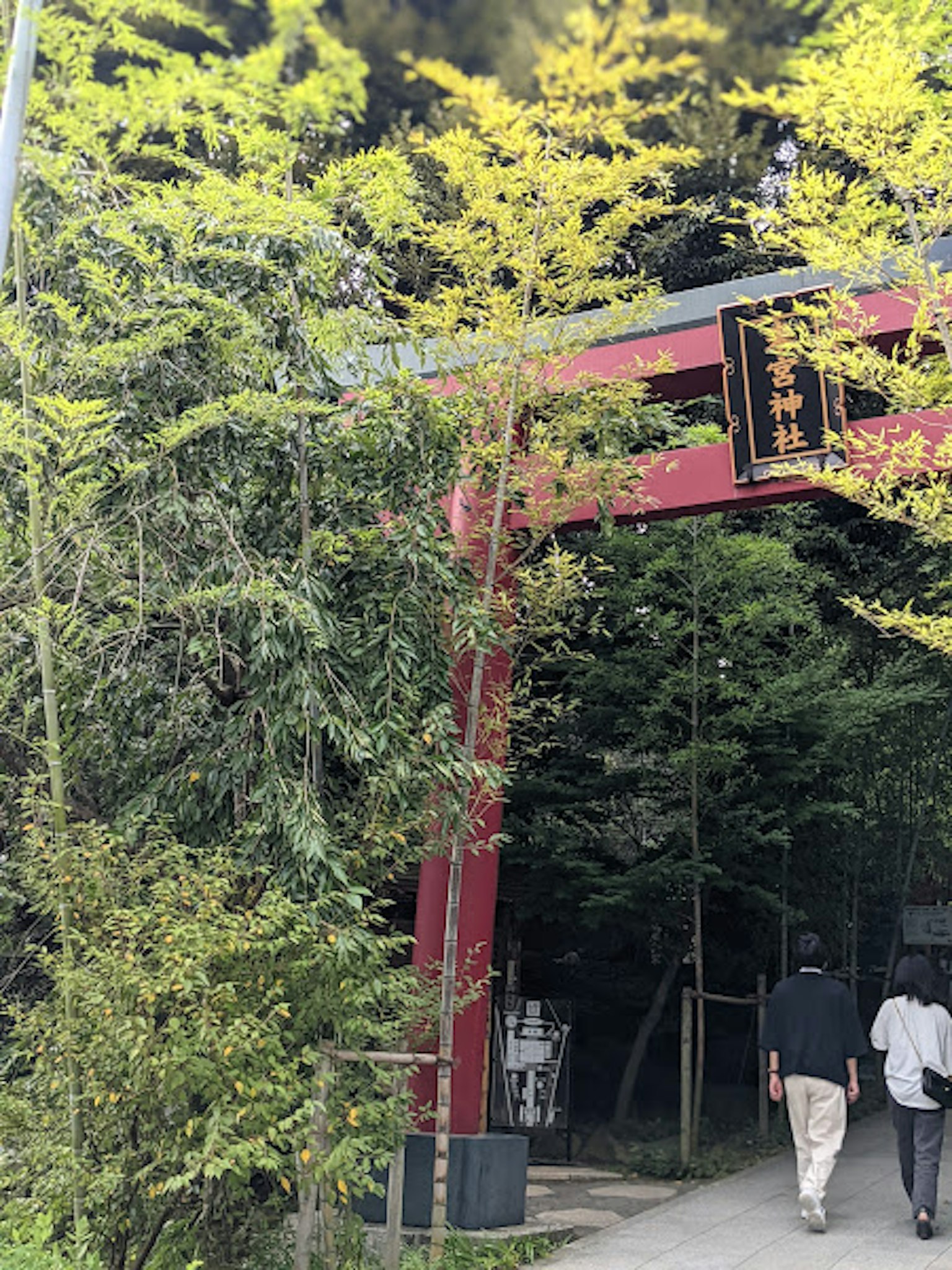 Scenic view of a red torii gate surrounded by greenery with people walking