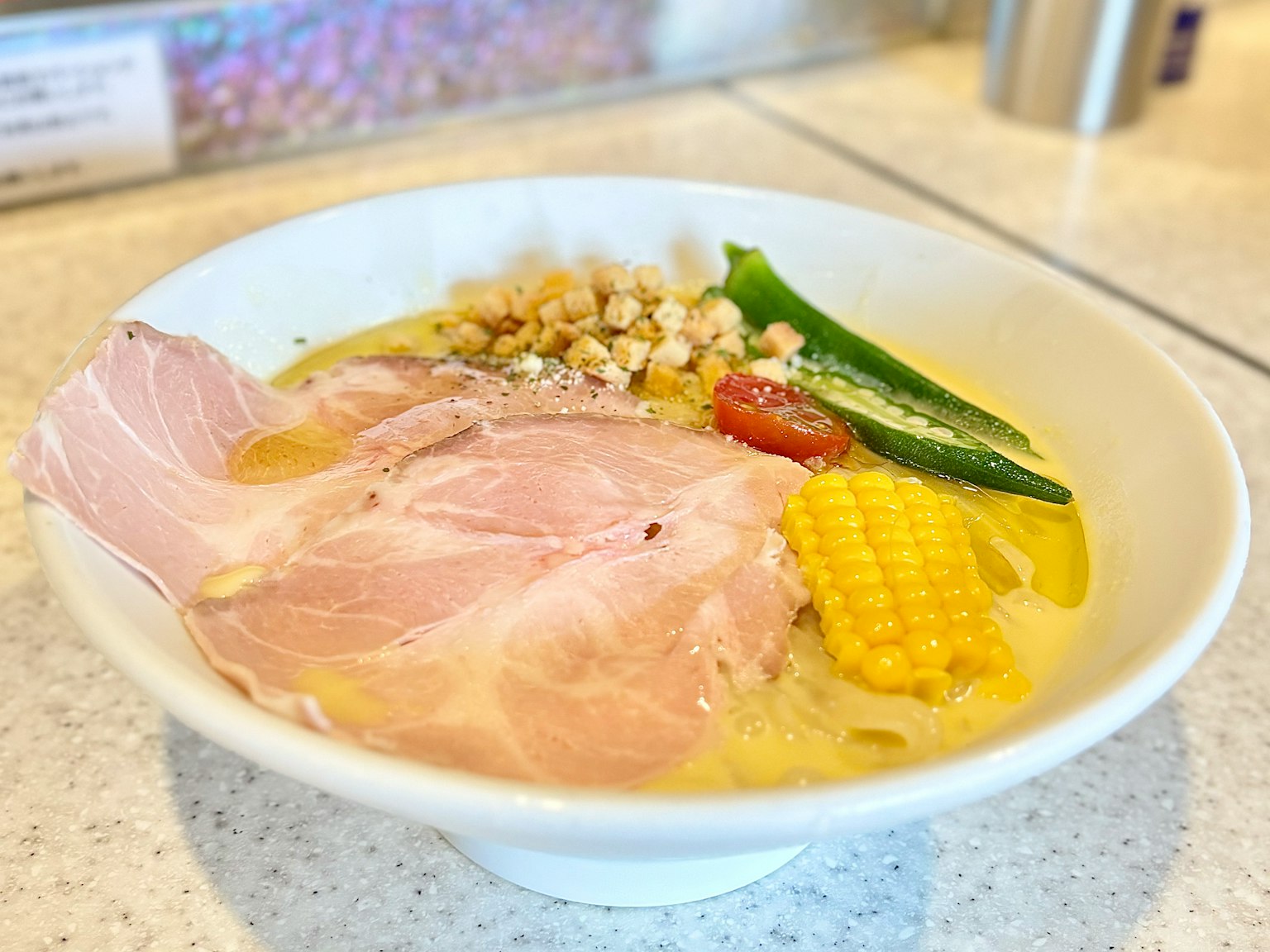 一碗拉面，上面放有猪肉片、玉米、秋葵、西红柿和坚果
