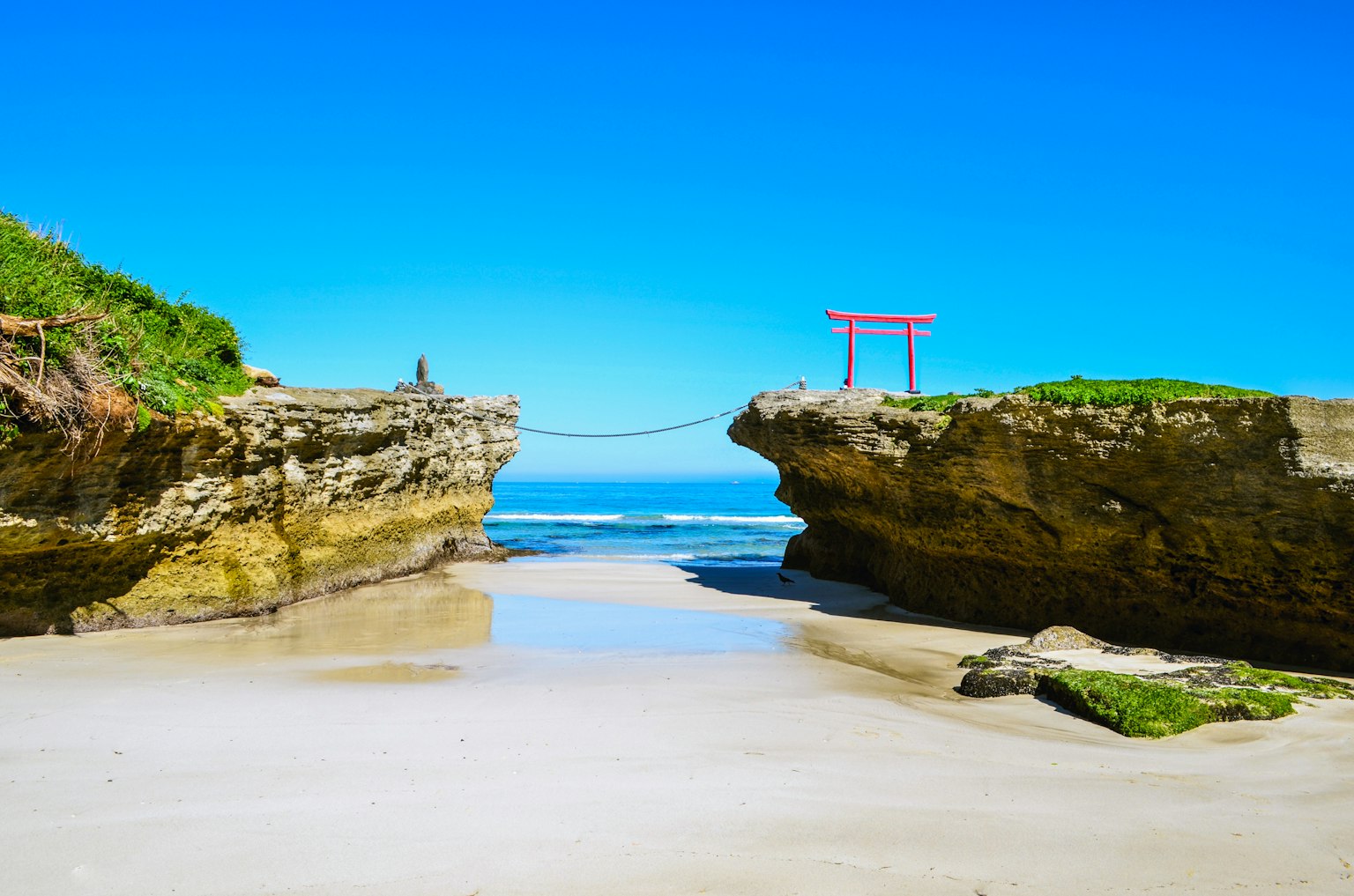 Vista panoramica di una spiaggia rocciosa con un torii rosso su uno sfondo di cielo blu