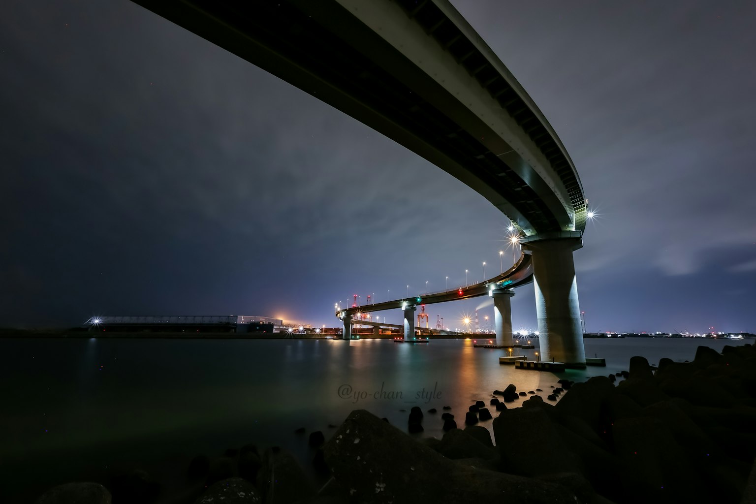 Vista da sotto un ponte sul mare di notte che mostra la struttura del ponte e le luci circostanti