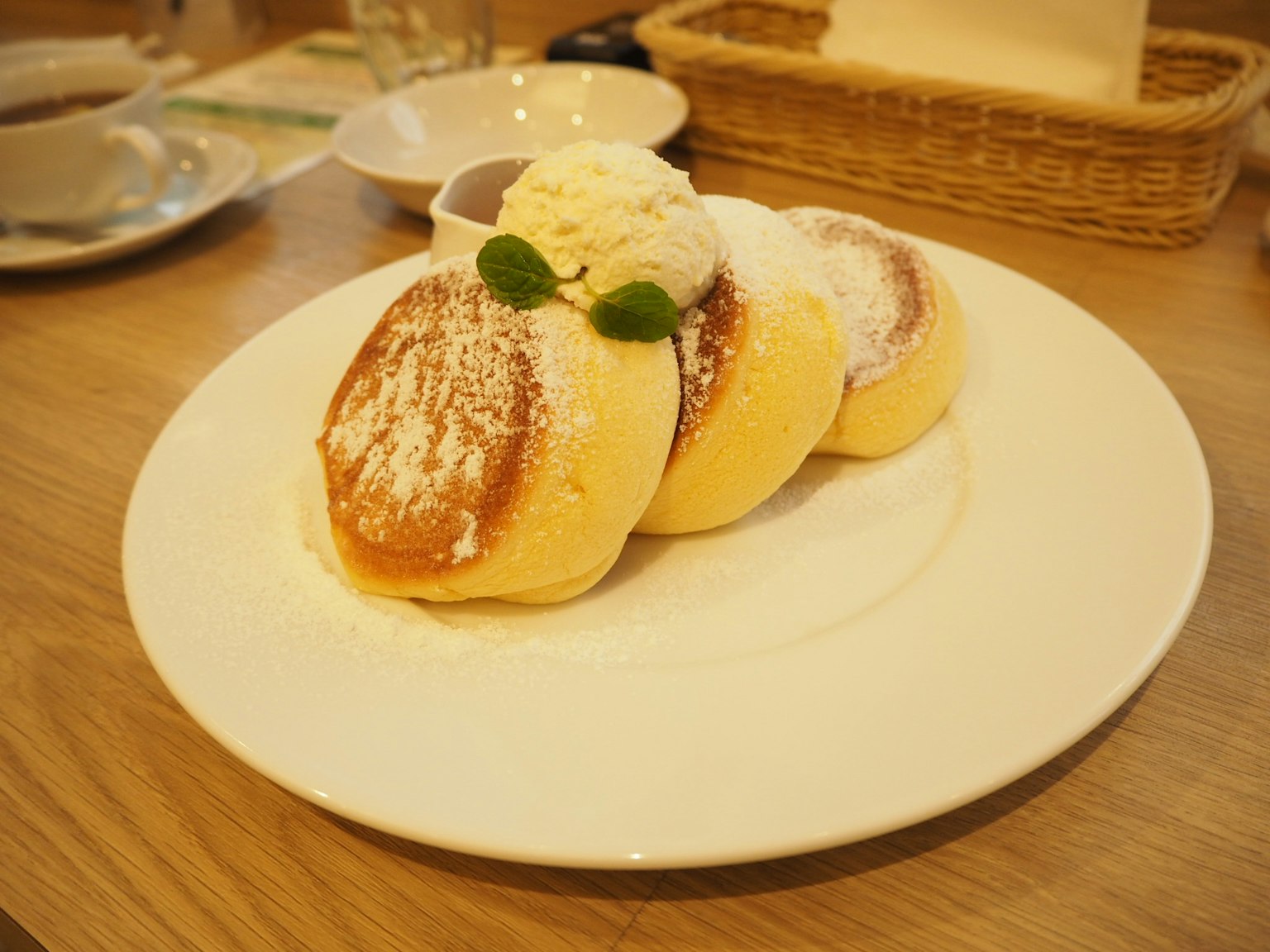 Tre pancake soffici guarniti con panna montata e una foglia di menta su un piatto bianco