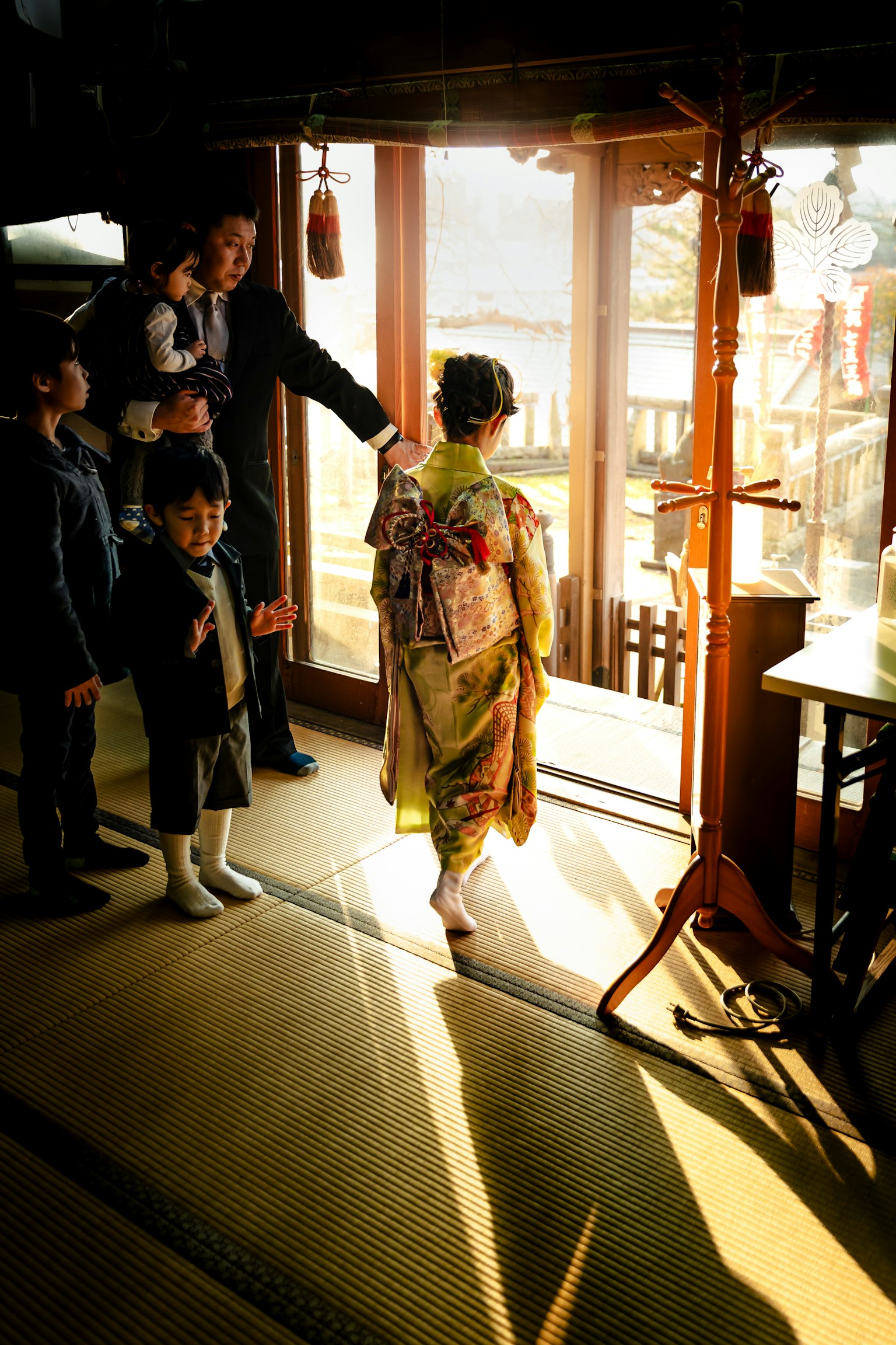 Kinder beobachten eine Frau im Kimono, die einen Raum verlässt, während Sonnenlicht durch das Fenster strömt