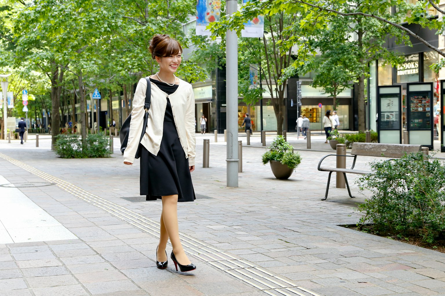 Femme en robe noire et veste blanche marchant dans un cadre urbain