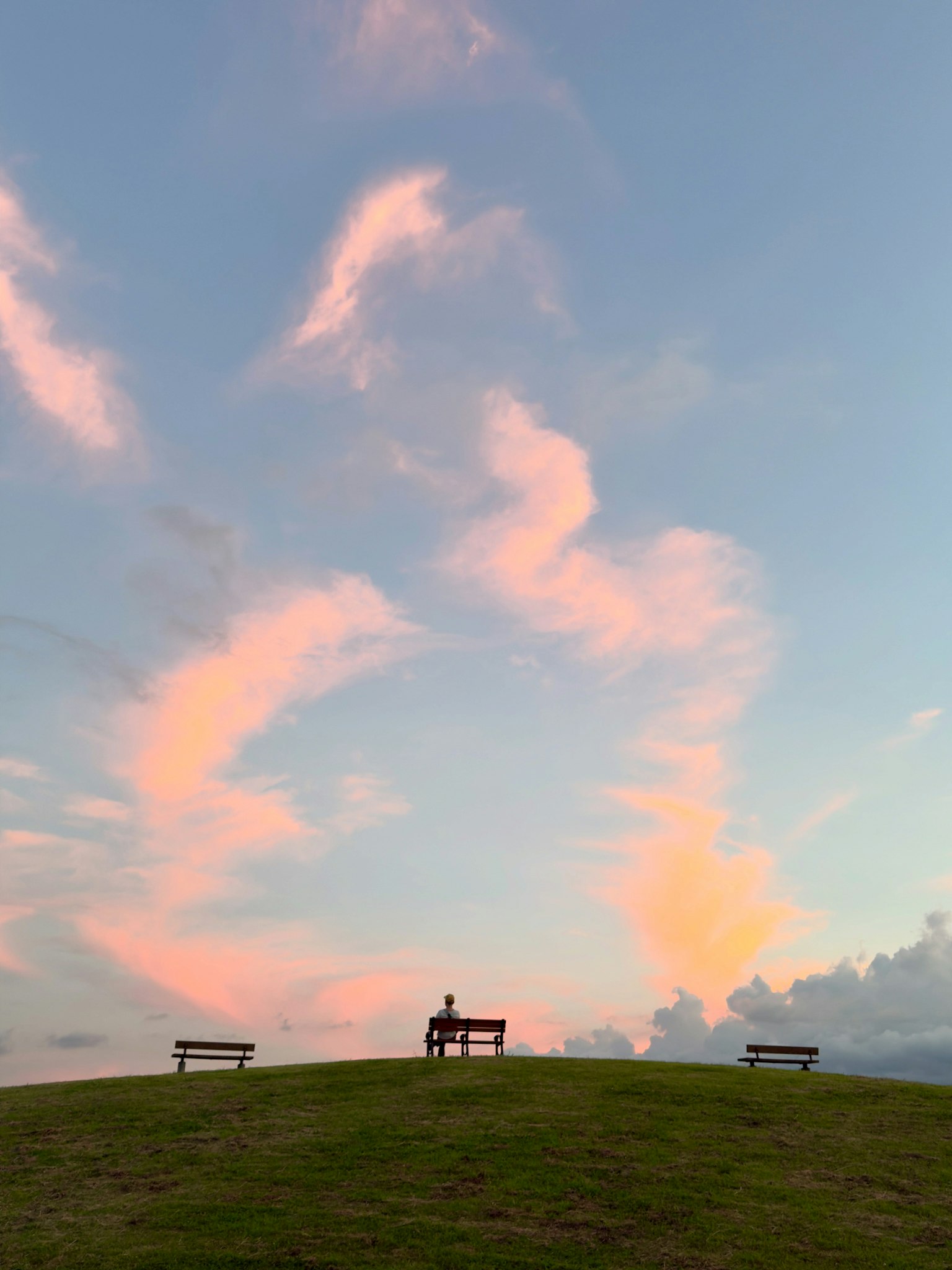 丘の上に座る人と色彩豊かな雲