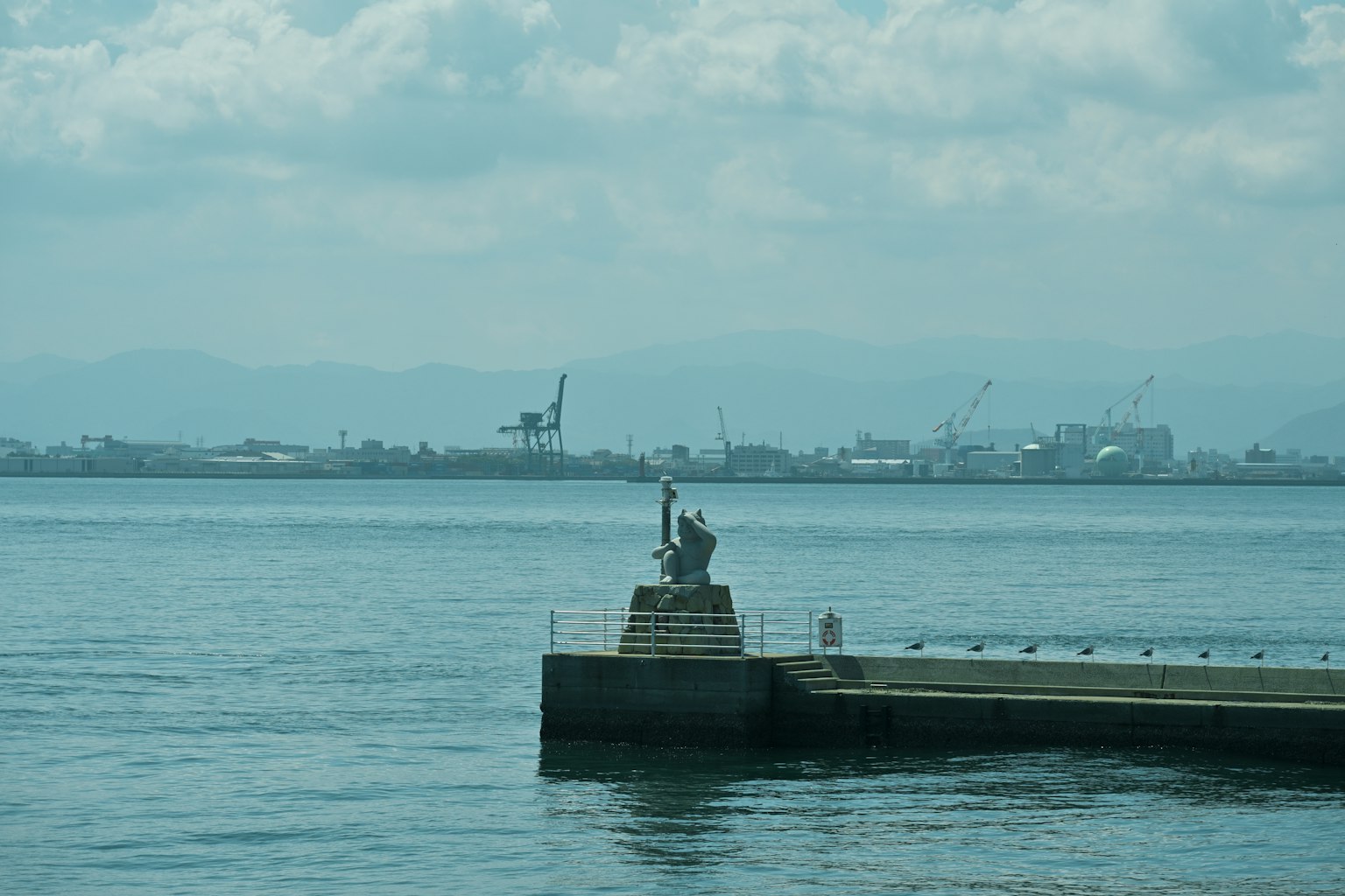 ทิวทัศน์เงียบสงบของท่าเรือที่มีรูปปั้นหันหน้าไปทางทะเล