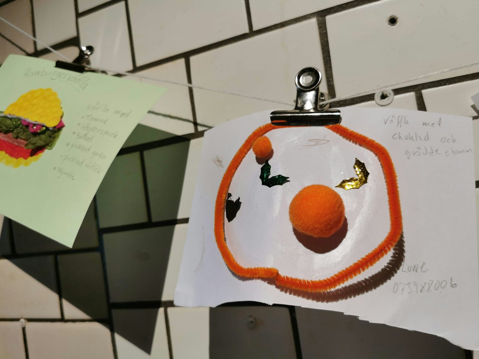 Artworks featuring a hamburger and an orange ball clipped to a tiled wall