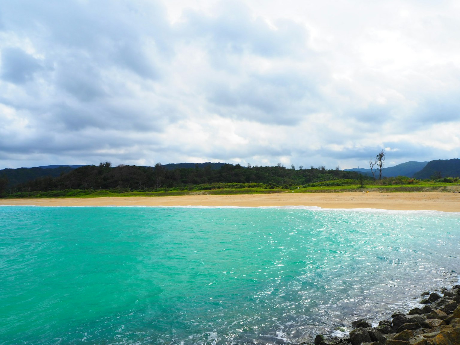 Vue pittoresque d'une eau turquoise et d'une plage de sable sous un ciel nuageux