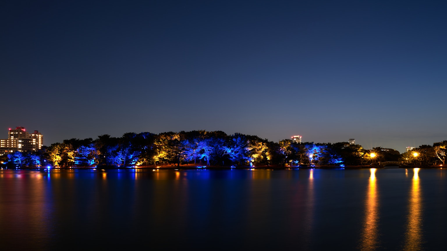 Hermosa escena nocturna con luces azules y naranjas reflejándose en un lago