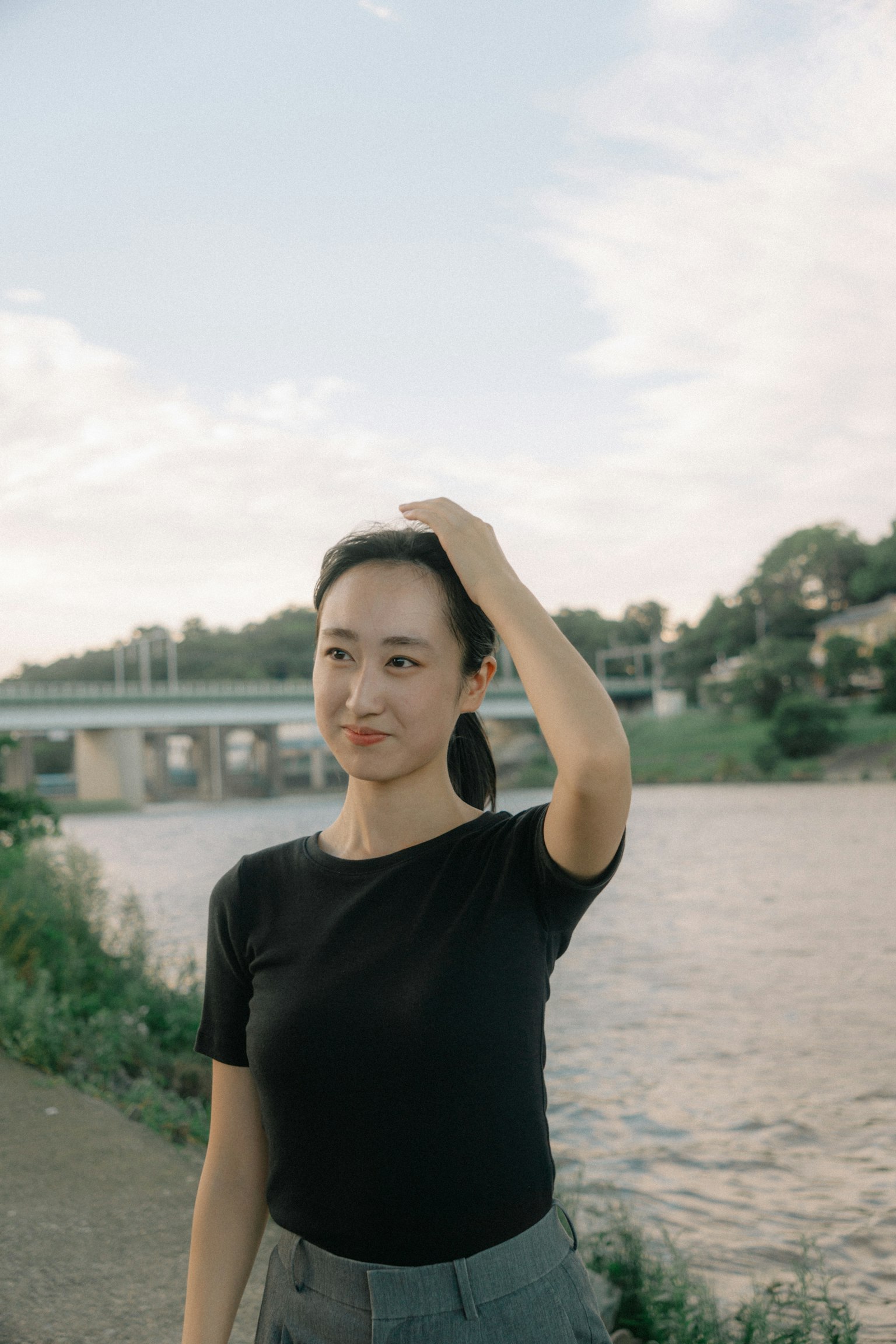 Eine Frau lächelt in der Nähe eines Flusses mit einer Brücke im Hintergrund