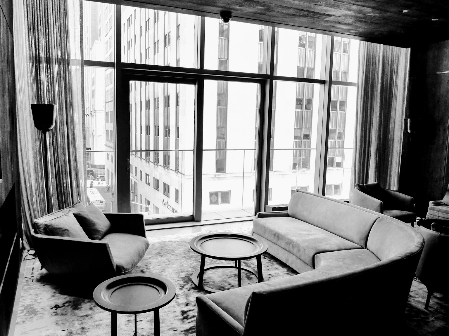Interior ruang tamu modern dengan sofa dan kursi hitam putih jendela besar membiarkan cahaya alami masuk