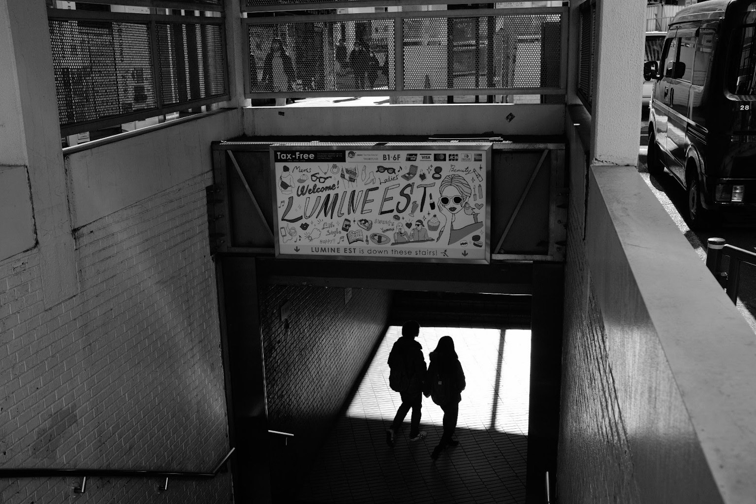 Dos figuras con sombras en la entrada de un paso subterráneo con un cartel colorido