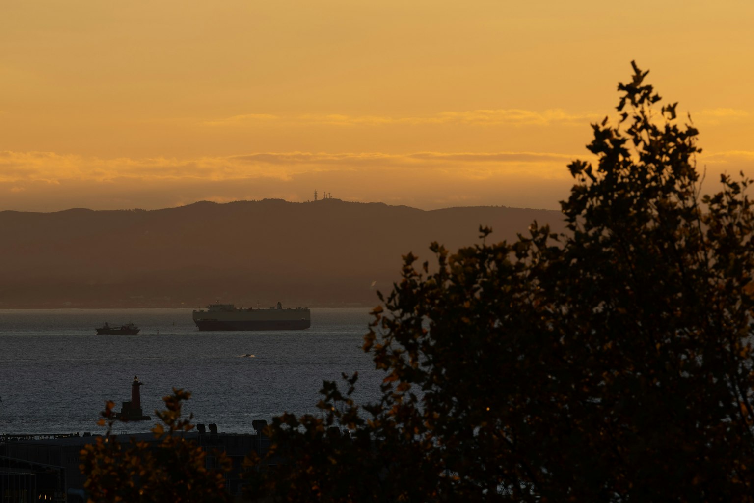 Silueta de barcos de carga en el mar al atardecer con montañas al fondo