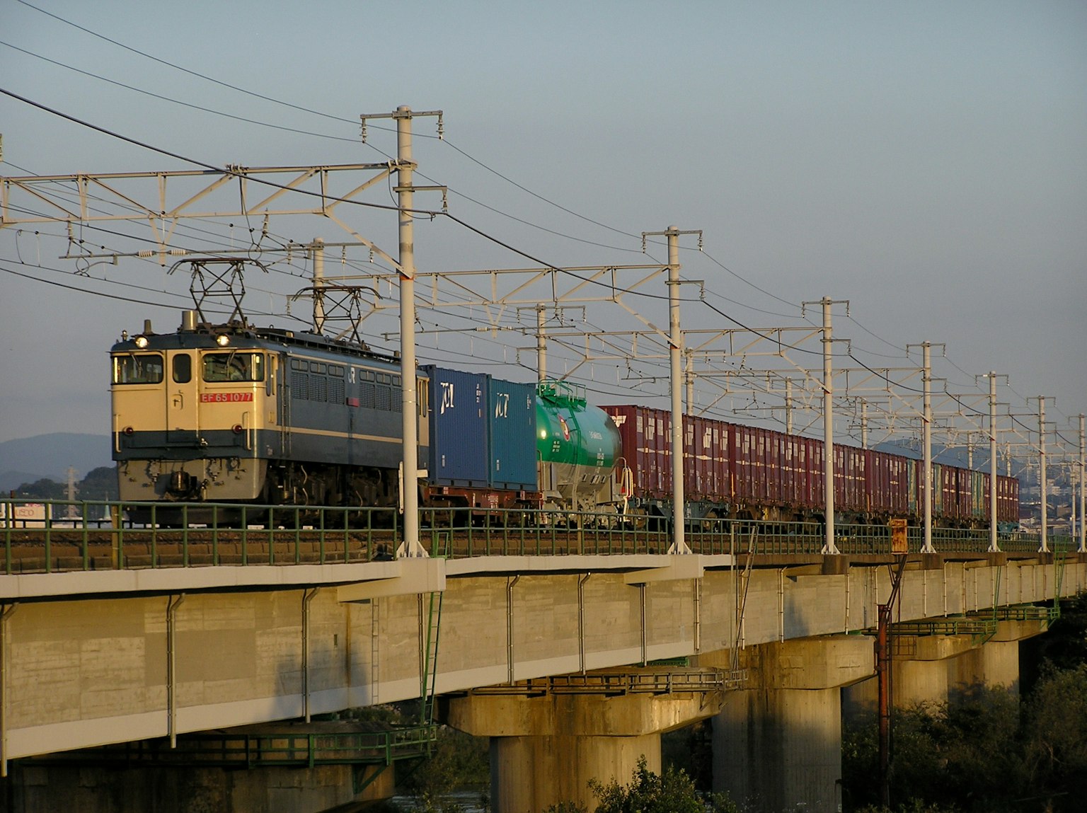 Tren de carga que circula sobre un puente con contenedores azules y verdes destacados