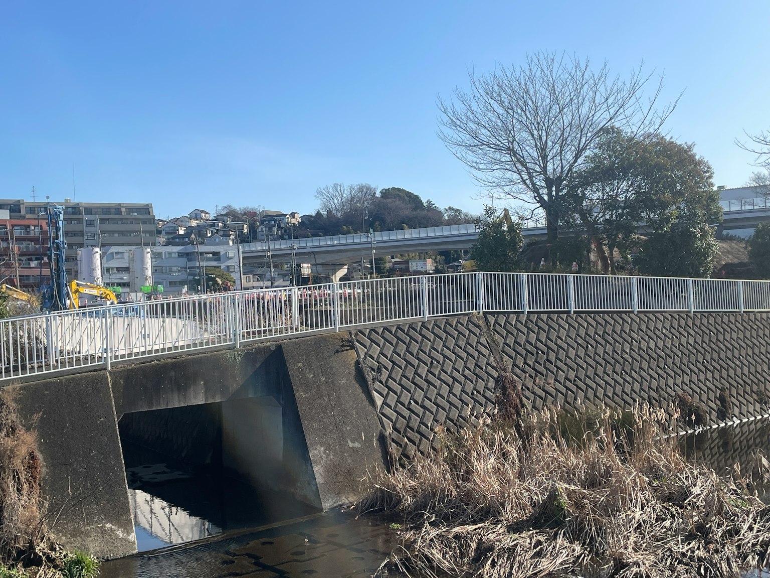 River with concrete embankment under blue sky and elevated railway