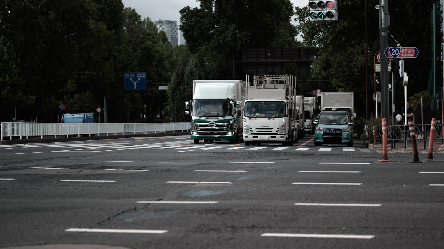 Des camions attendant à un carrefour avec des arbres verts et des feux de circulation en arrière-plan