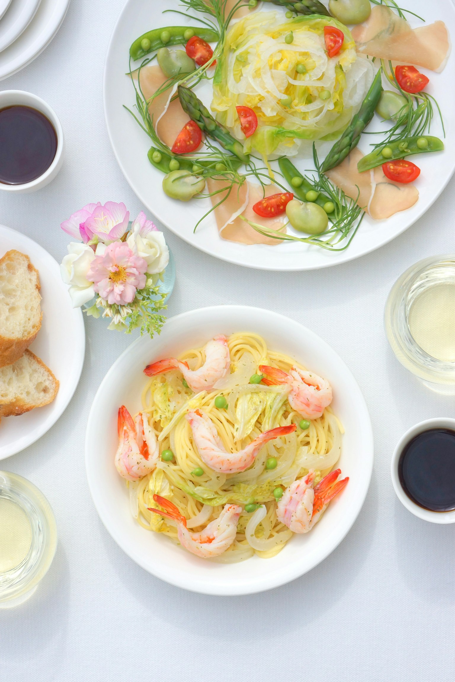 Una ciotola di pasta con gamberi e limone con un'insalata guarnita con verdure fresche e prosciutto su un piatto bianco