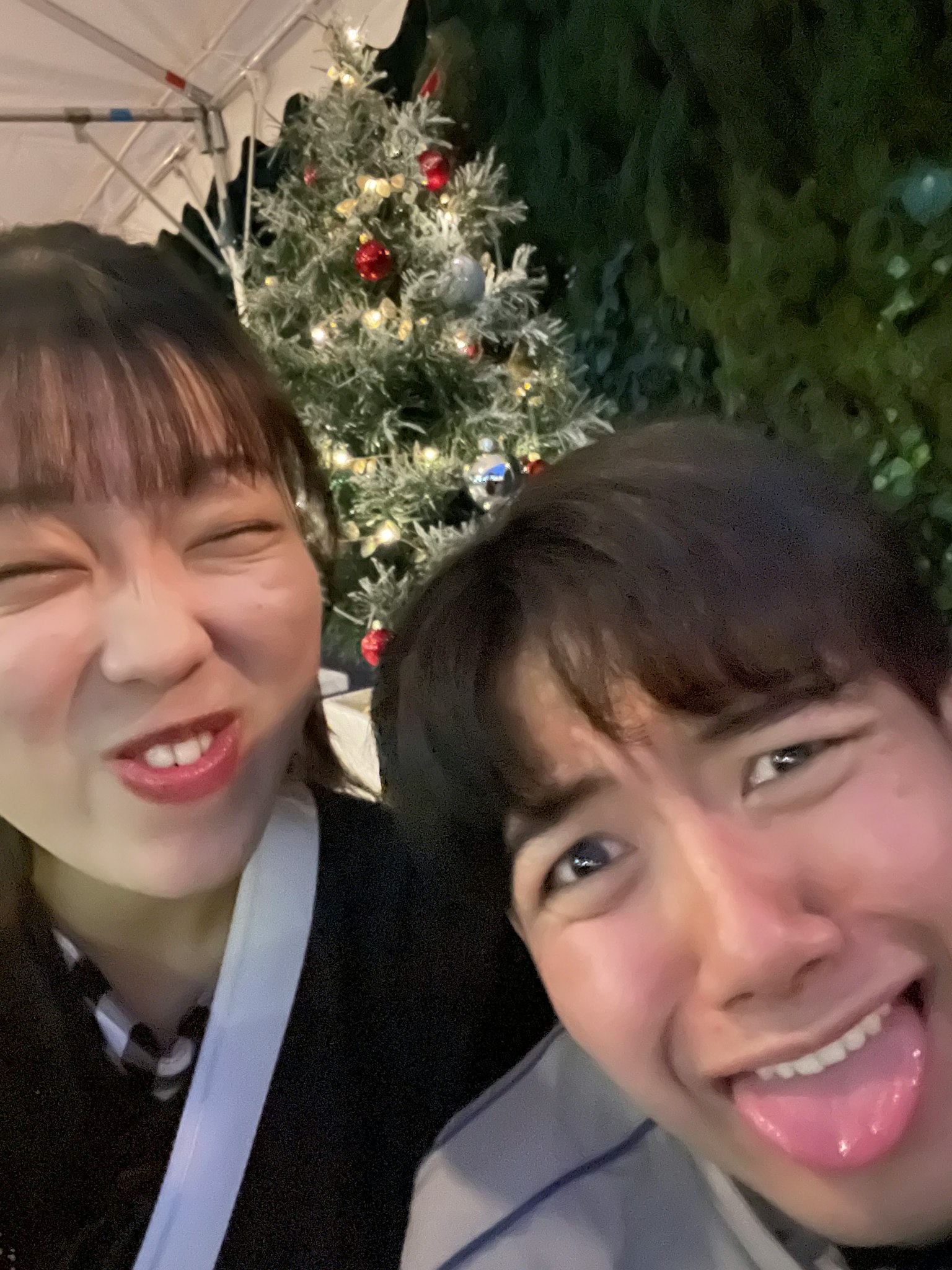 Dos jóvenes haciendo caras graciosas frente a un árbol de Navidad